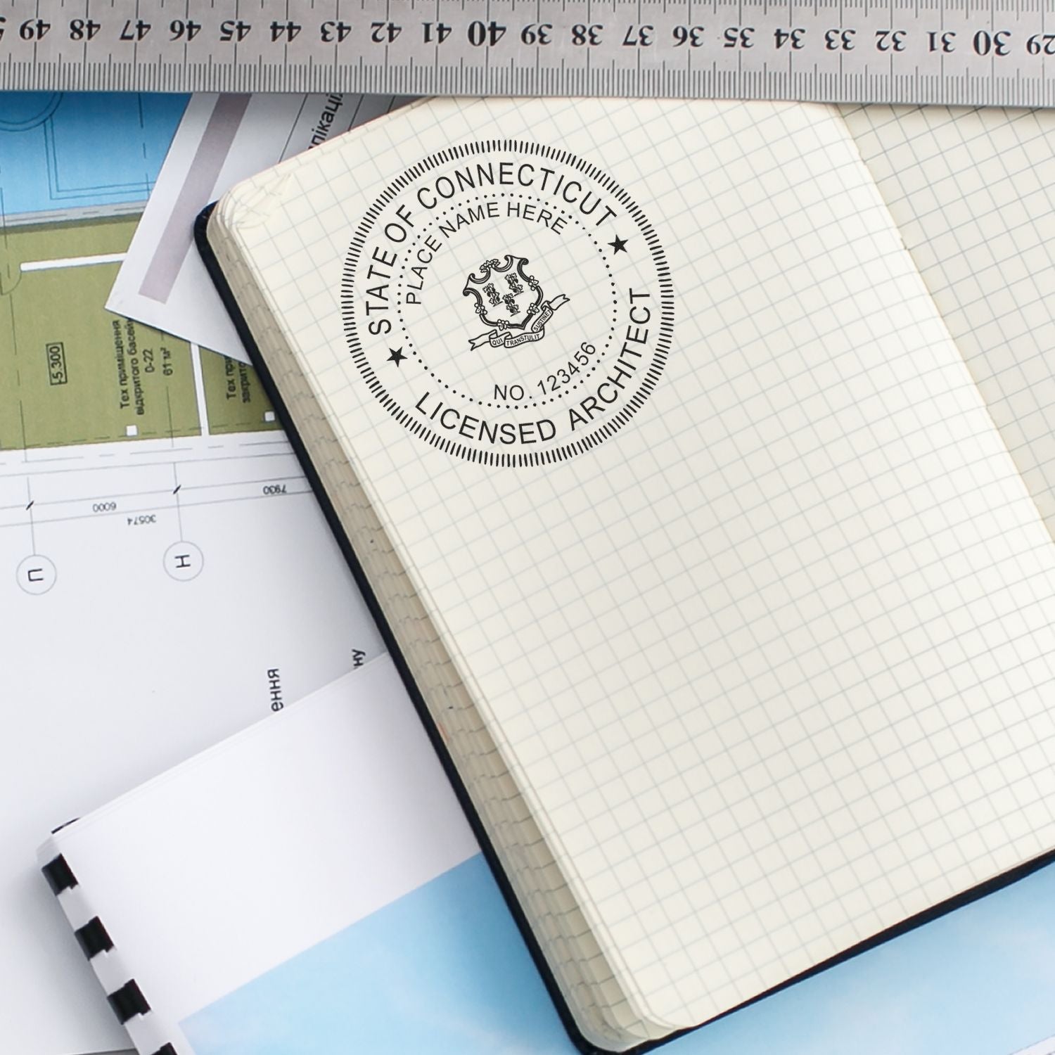 Self Inking Connecticut Architect Stamp used on a grid notebook, surrounded by architectural plans and a ruler.