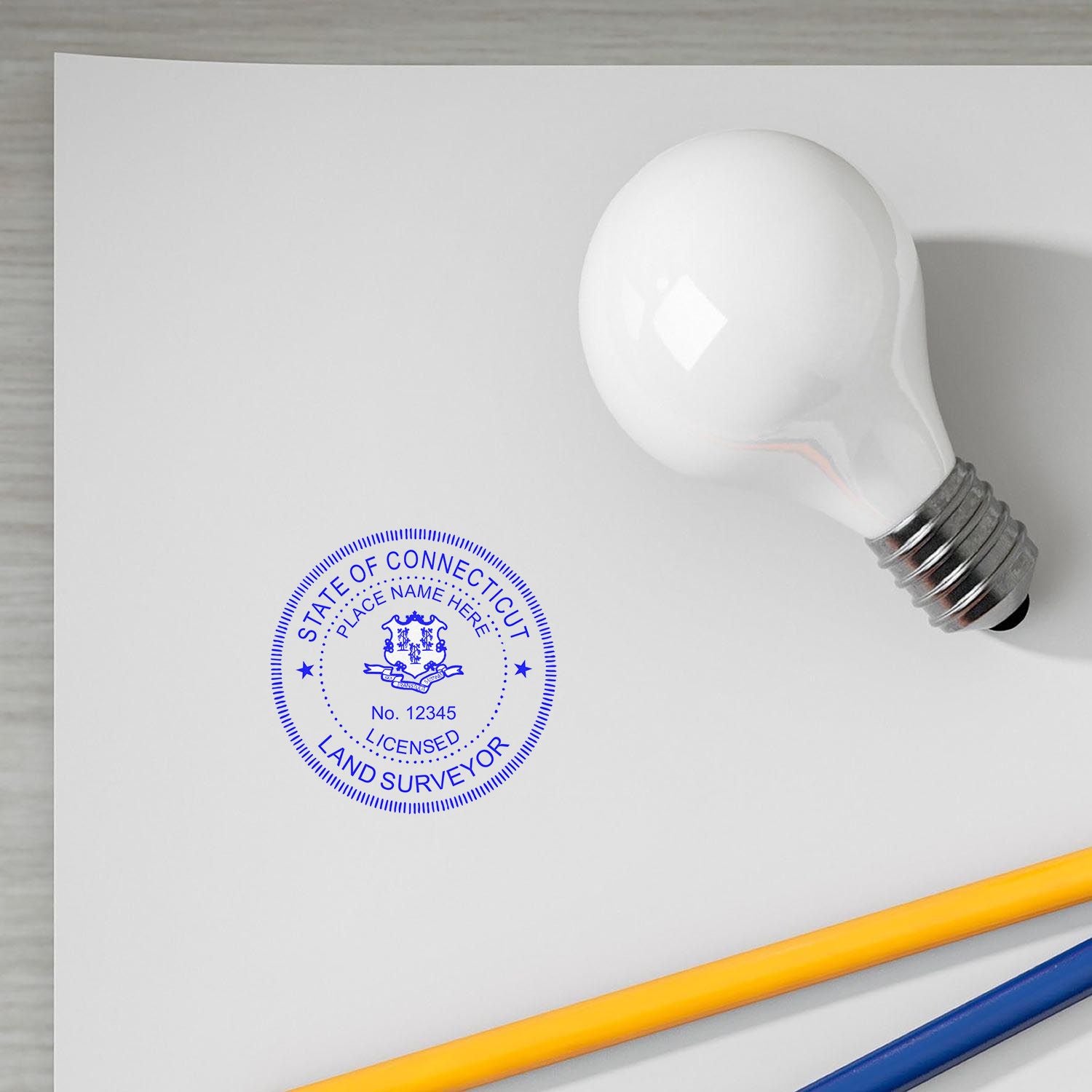 Connecticut Land Surveyor Seal Stamp on white paper next to a light bulb and pencils.