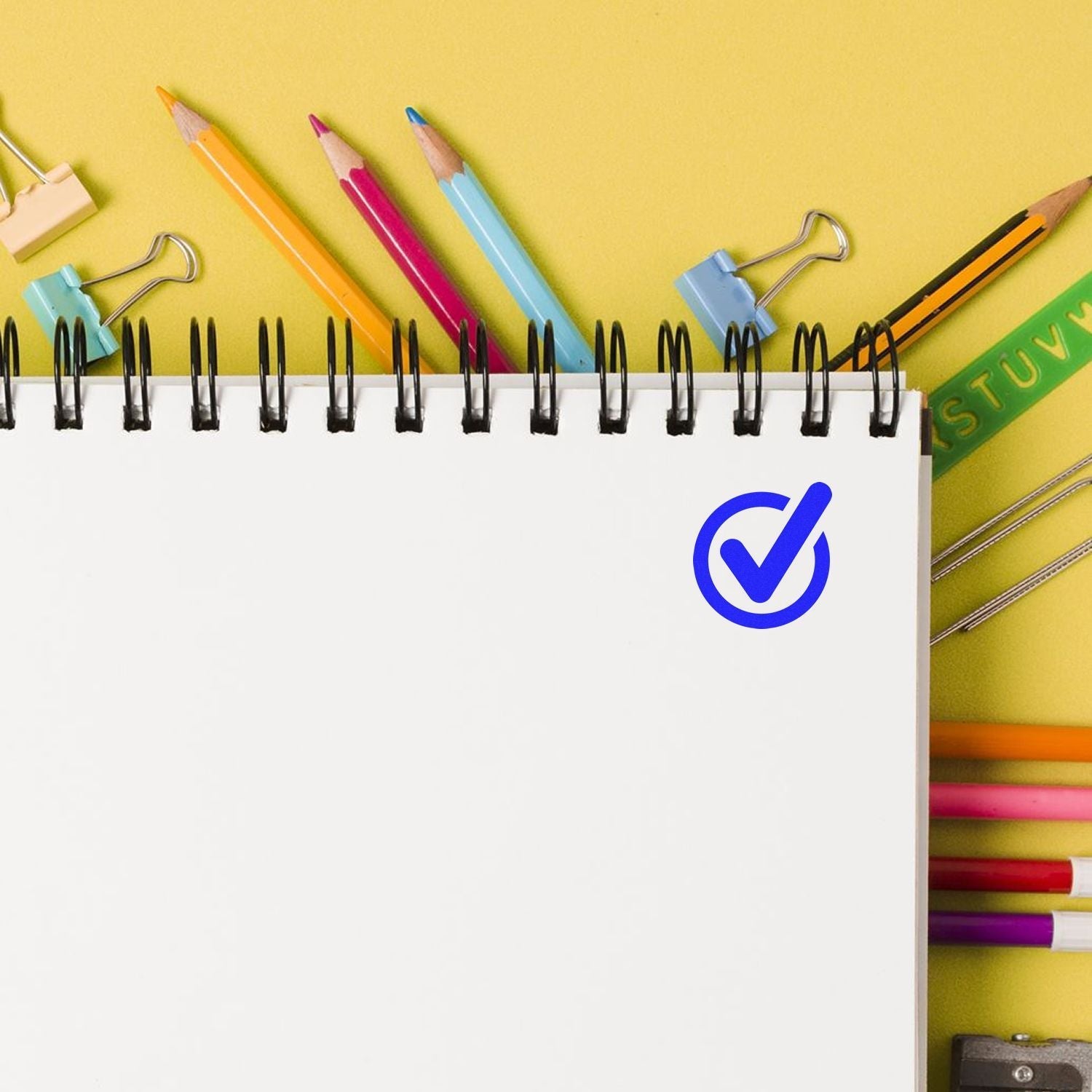 A Custom Self Inking Stamp Trodat 4612 Size 1/2 Diameter is used to stamp a blue checkmark on a white notebook page surrounded by colorful stationery.