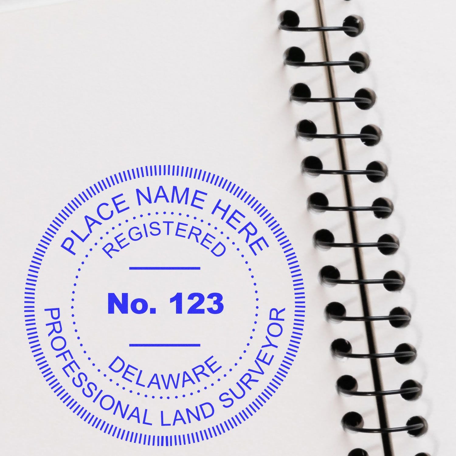 Self Inking Delaware Land Surveyor Stamp imprint on a white spiral-bound notebook, showing PLACE NAME HERE and No. 123 in blue ink.