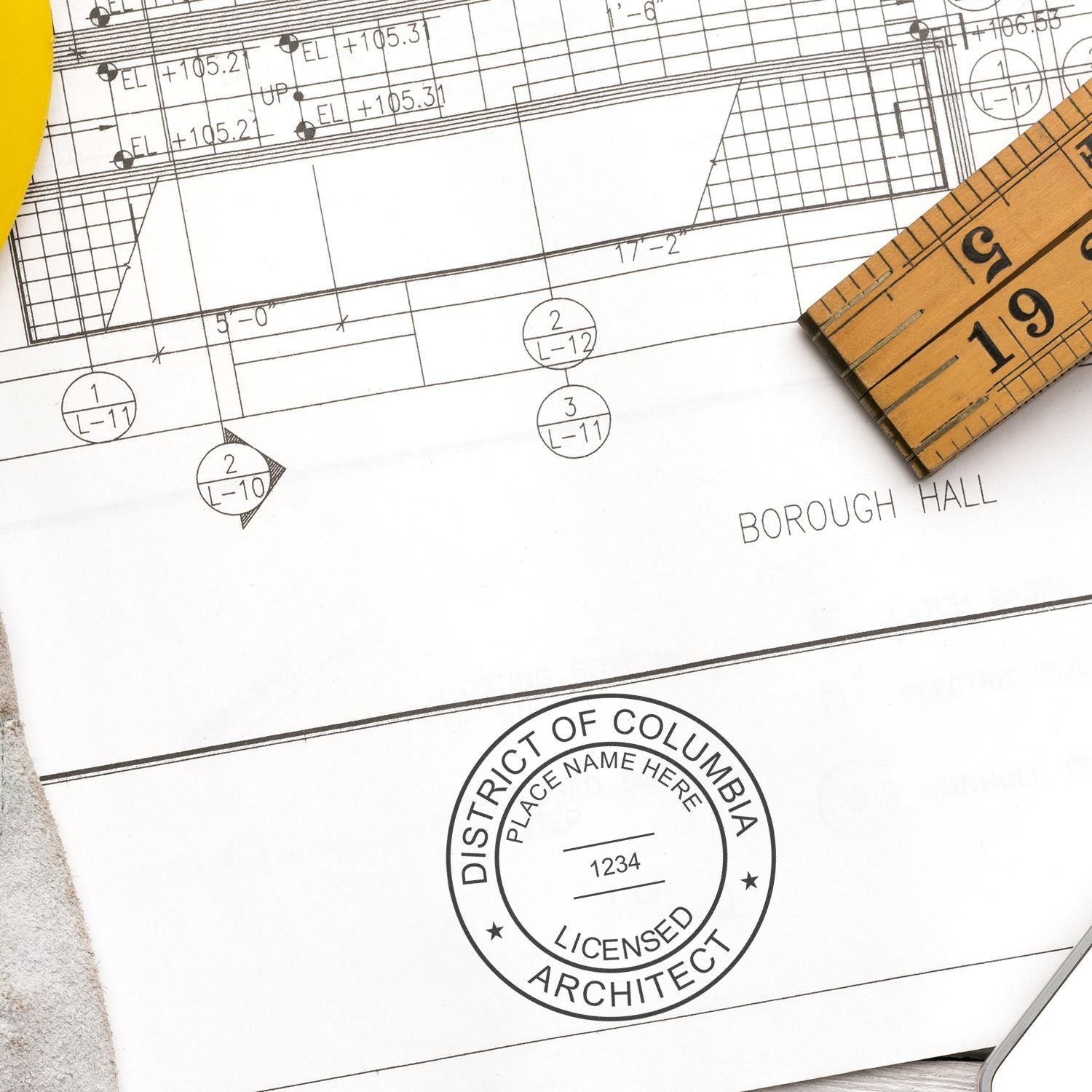 District of Columbia Architect Seal Stamp on architectural blueprint with a ruler and yellow tool in the background.