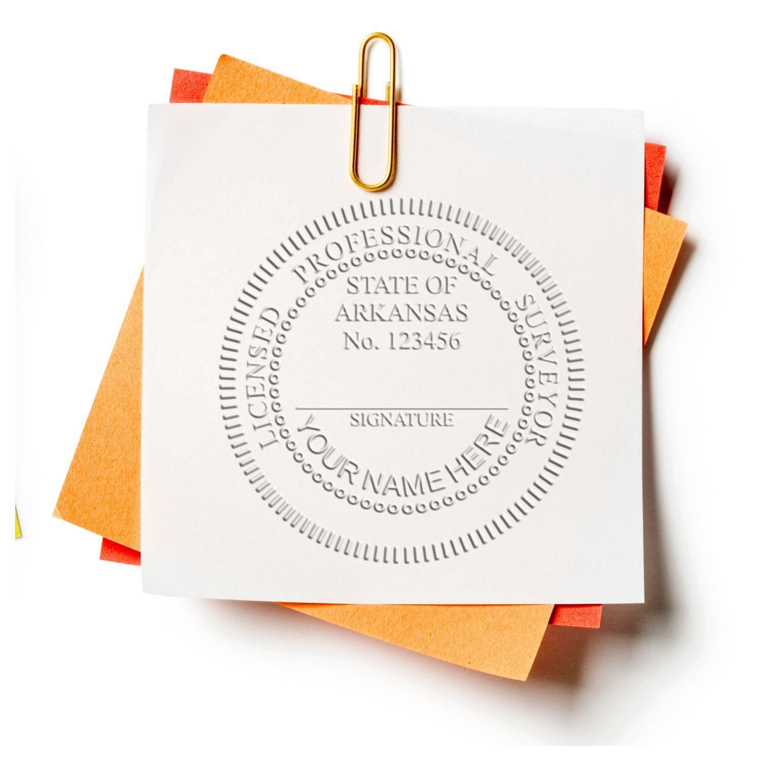 Land Surveyor Long Reach Desk Seal Embosser in use, showing an embossed seal on a white paper clipped to orange and yellow papers.