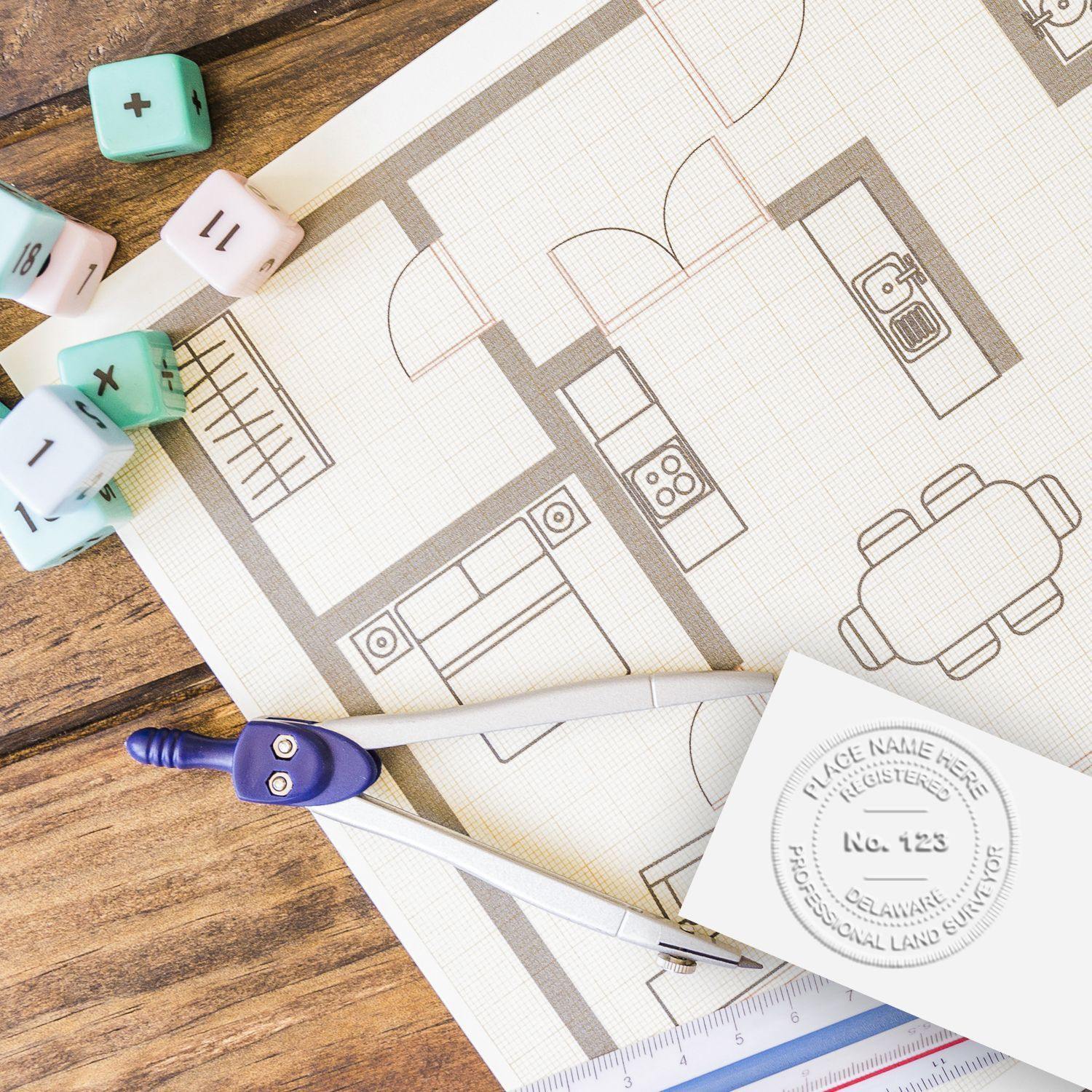 Land Surveyor Cast Iron Desk Seal Embosser in use on a floor plan, surrounded by drafting tools and pastel-colored dice on a wooden desk.