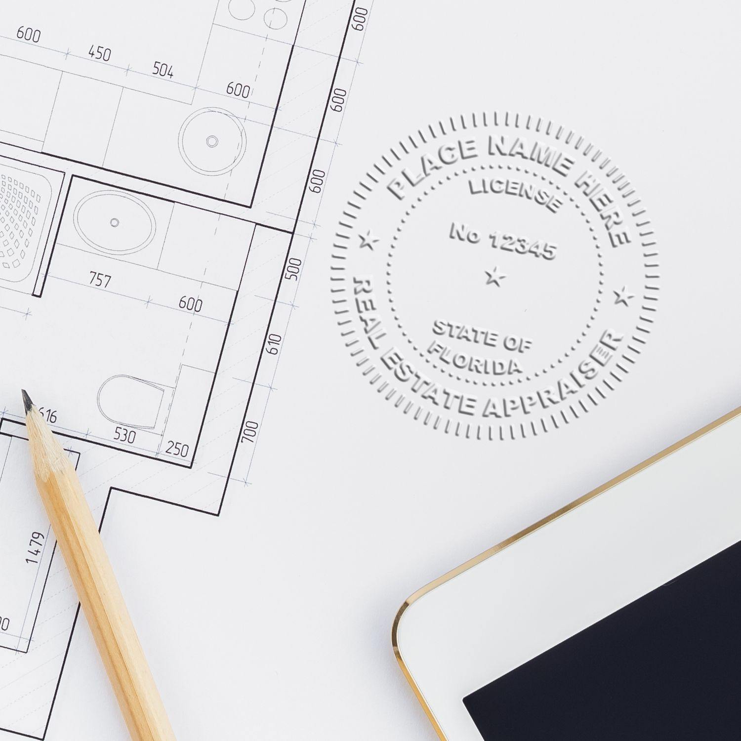 Real Estate Appraiser Handheld Seal Embosser in use on architectural plans, next to a pencil and tablet.