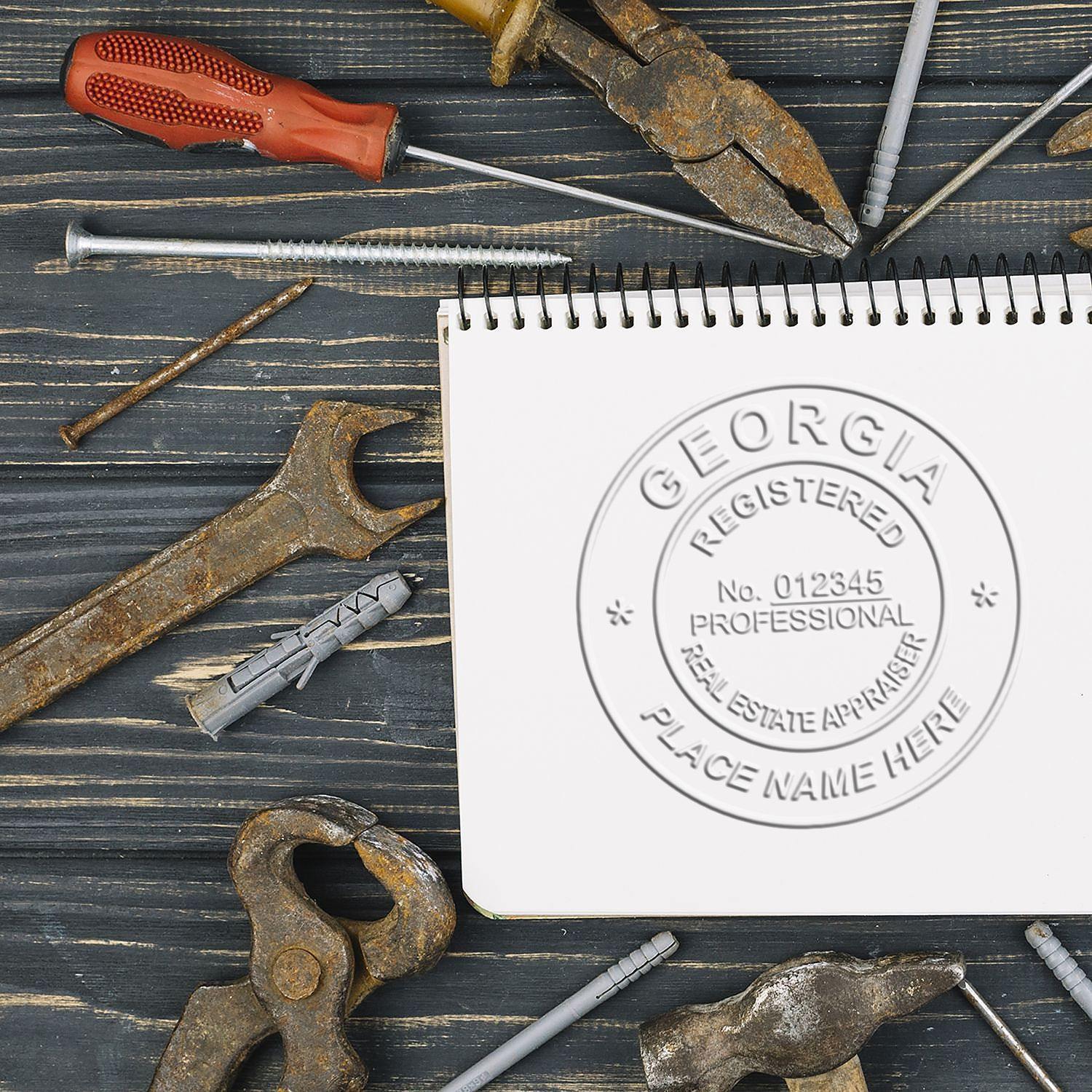 Real Estate Appraiser Chrome Gift Seal Embosser imprint on a notebook, surrounded by various rusty tools on a wooden surface.