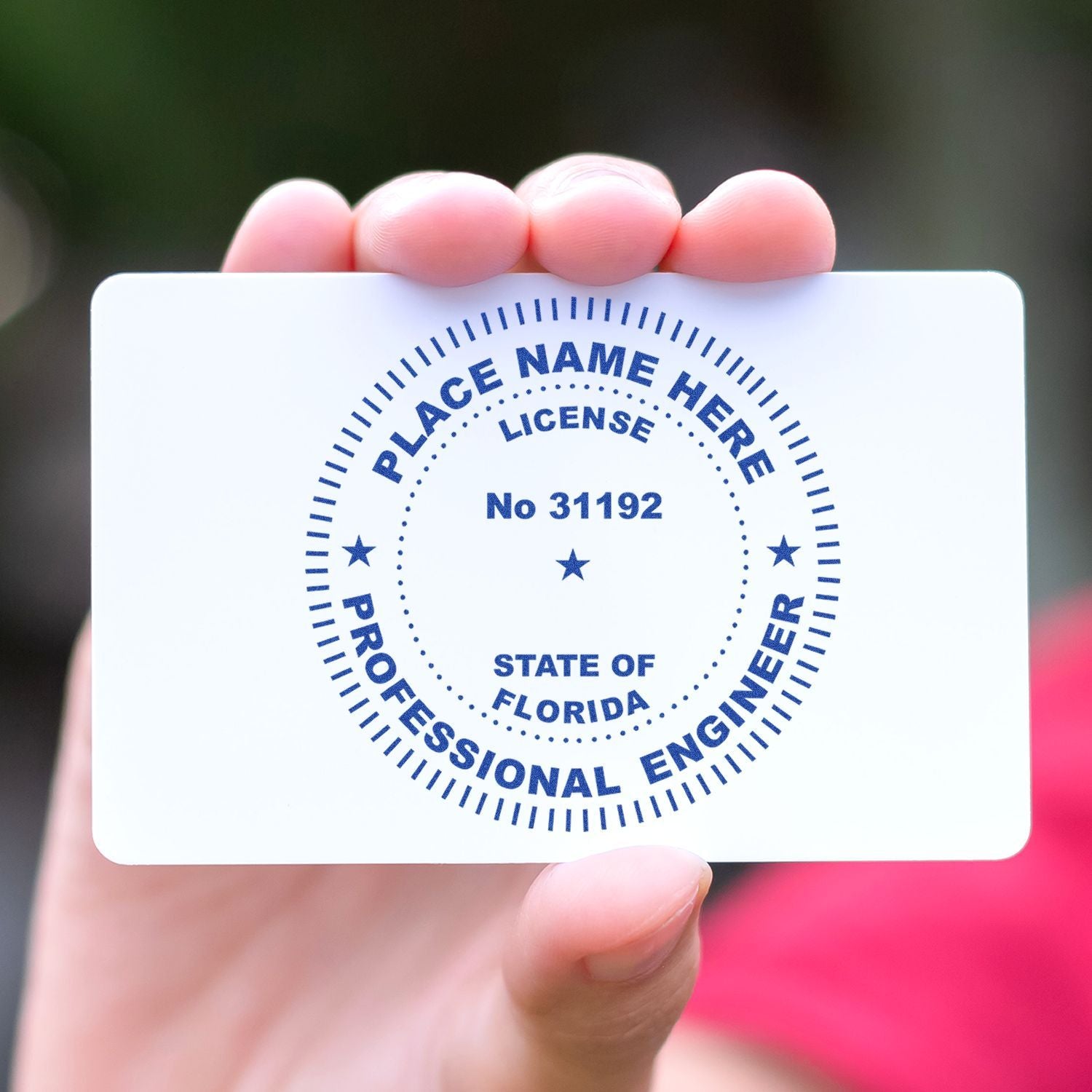 A hand holding a white card with a blue circular stamp that reads PLACE NAME HERE, LICENSE No 31192, STATE OF FLORIDA, PROFESSIONAL ENGINEER. This is the Professional Engineer eSeal Electronic Image Stamp of Seal.