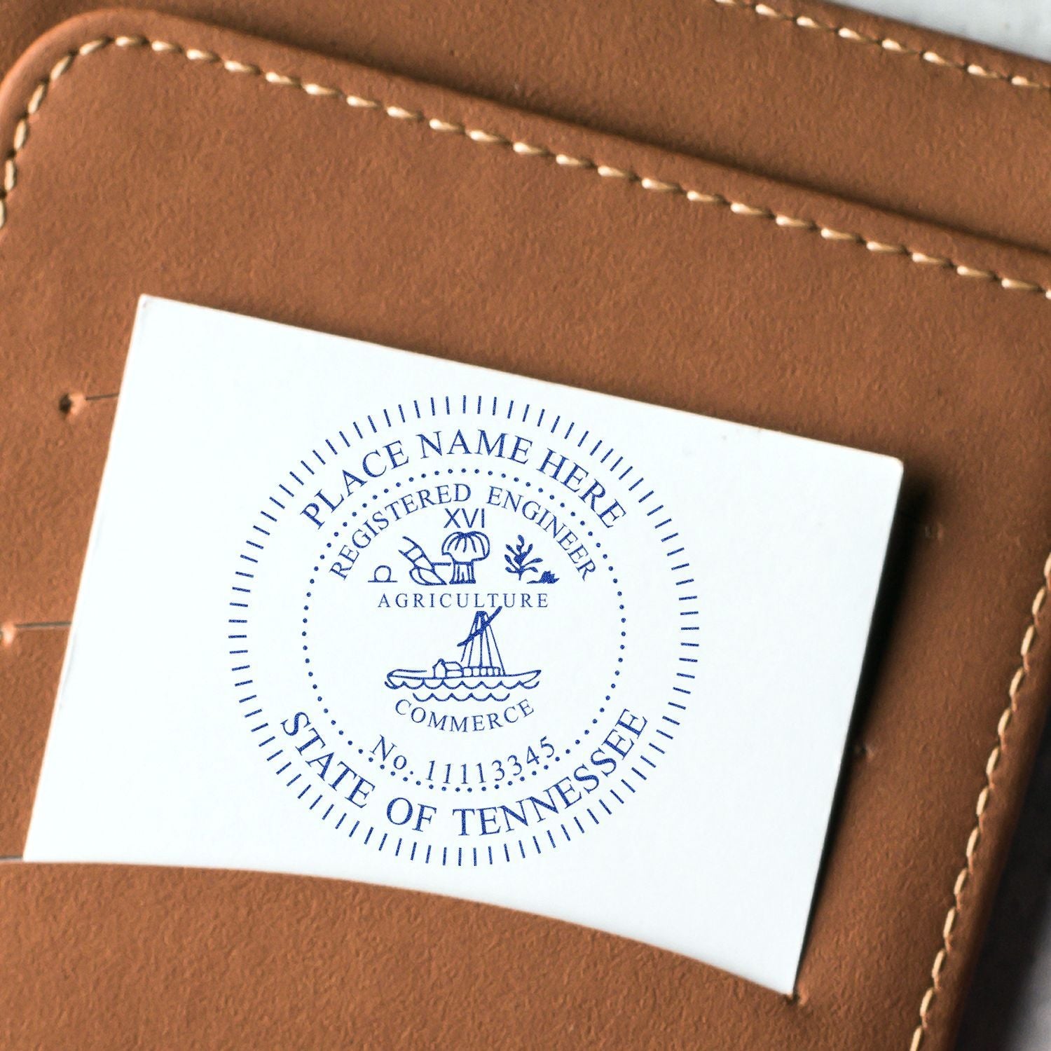 A close-up of a tan leather wallet with a white card displaying a blue imprint from the Professional Engineer Slim Pre-Inked Stamp of Seal, featuring a detailed design and text for a registered engineer.