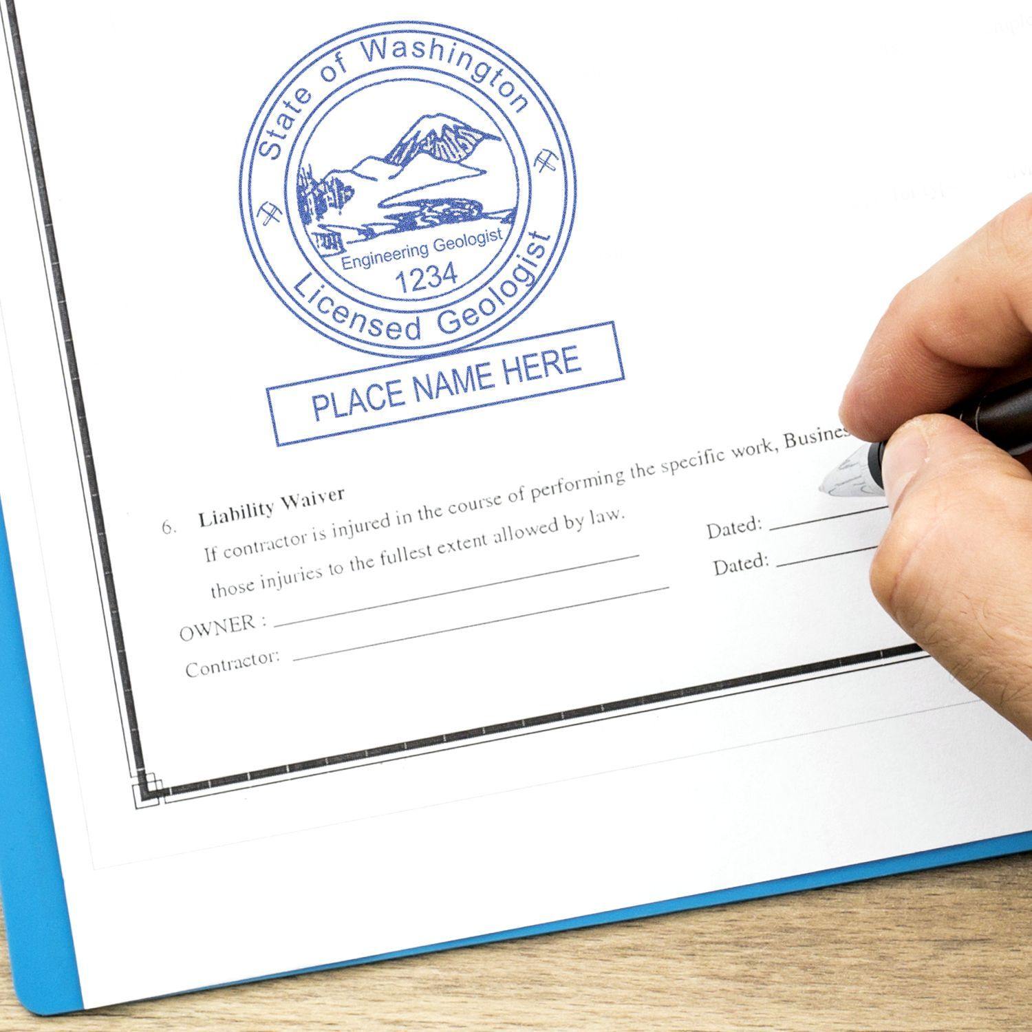 A hand holding a pen next to a stamped document with the Engineering Geologist Regular Rubber Stamp of Seal, displaying a circular seal with State of Washington Licensed Geologist and space for a name.