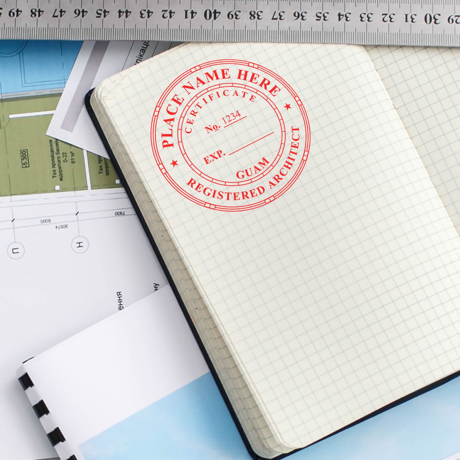 Premium MaxLight Pre-Inked Guam Architectural Stamp in red ink on a grid notebook, surrounded by architectural plans and a ruler.