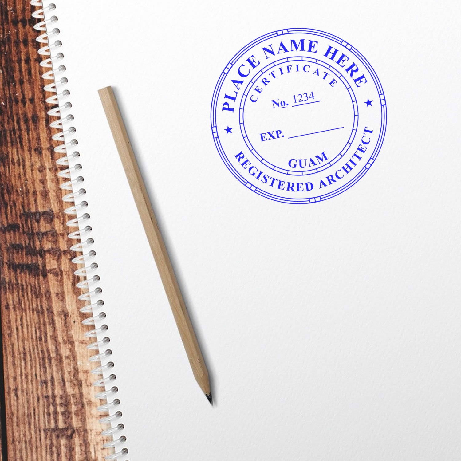 Self Inking Guam Architect Stamp in blue ink on white paper, next to a wooden pencil on a spiral-bound notebook.