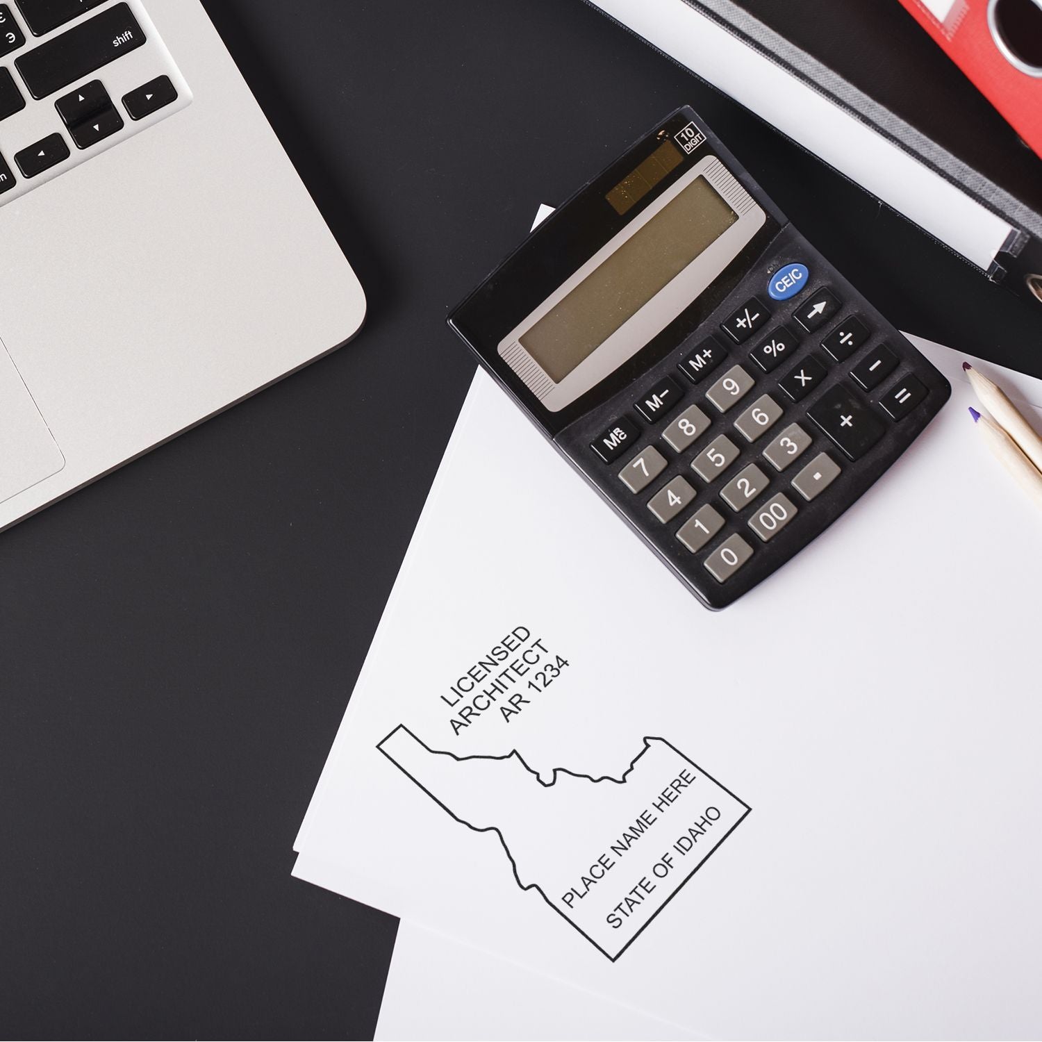 Self Inking Idaho Architect Stamp on paper next to a calculator, pencil, and laptop on a black desk.