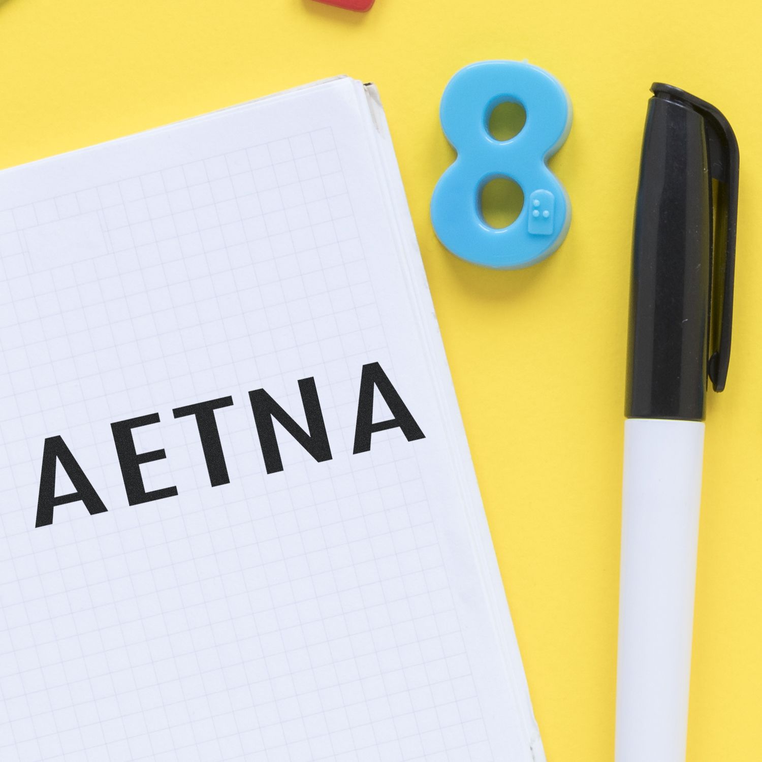 Large Aetna Rubber Stamp in use on a grid notebook, with a black pen and a blue number 8 magnet on a yellow background.