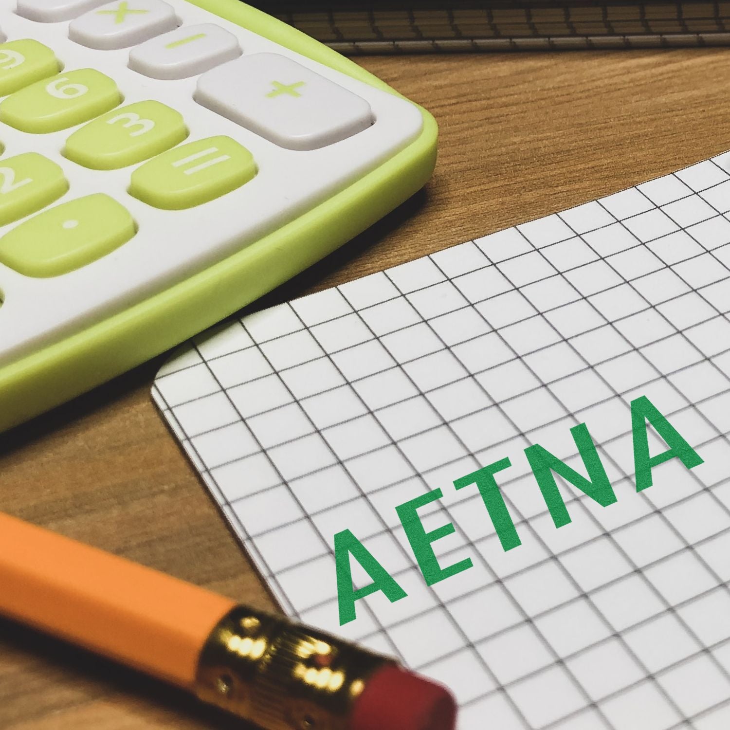 Large Pre-Inked Aetna Stamp used on graph paper next to a green calculator and a pencil with an eraser on a wooden desk.