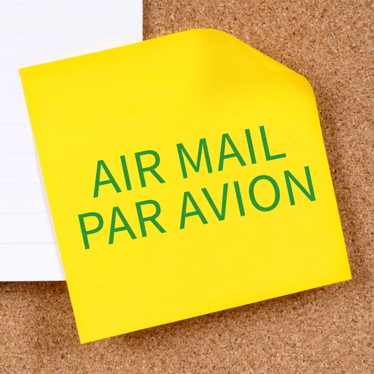 Yellow sticky note stamped with AIR MAIL PAR AVION using the Self Inking Air Mail Par Avion Stamp, placed on a corkboard.