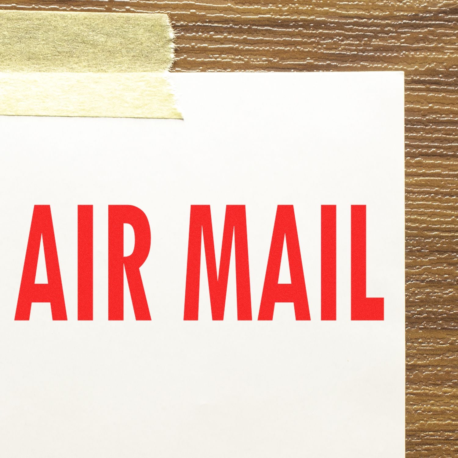 Close-up of a white envelope with AIR MAIL stamped in red using the Self Inking Air Mail Stamp, taped to a wooden surface.