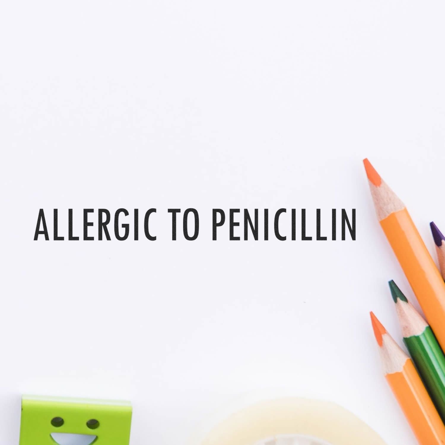 Large Pre-Inked Allergic To Penicillin Stamp in use on white paper, surrounded by colorful pencils, an eraser, and tape.