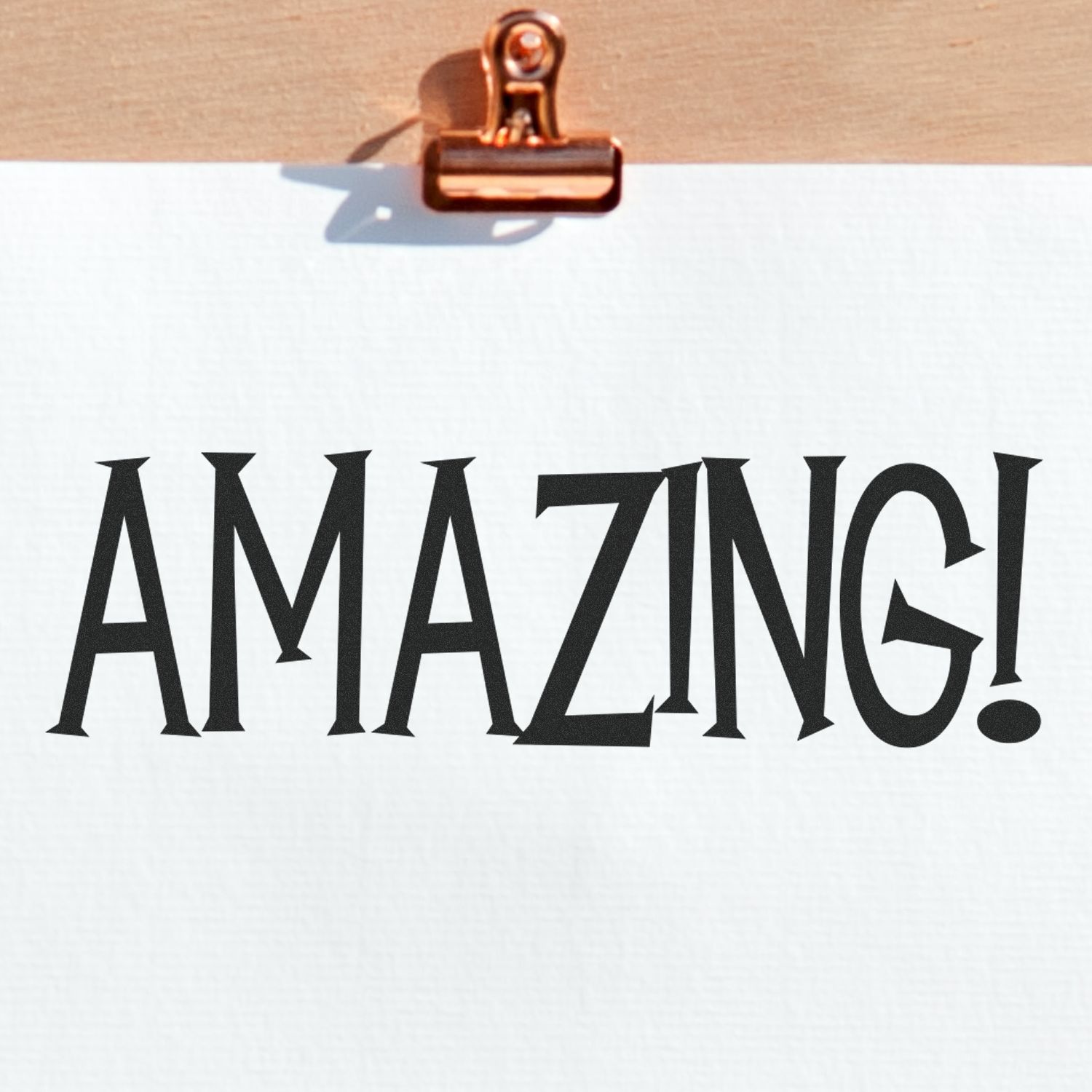 A piece of paper stamped with the word AMAZING! using the Large Amazing Rubber Stamp, clipped to a wooden board.