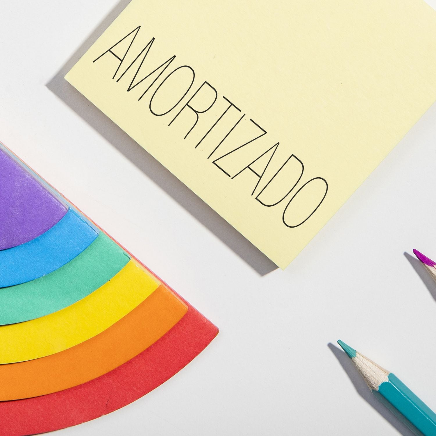 A yellow paper stamped with AMORTIZADO using the Self Inking Amortizado Stamp, next to colorful paper and pencils on a white surface.