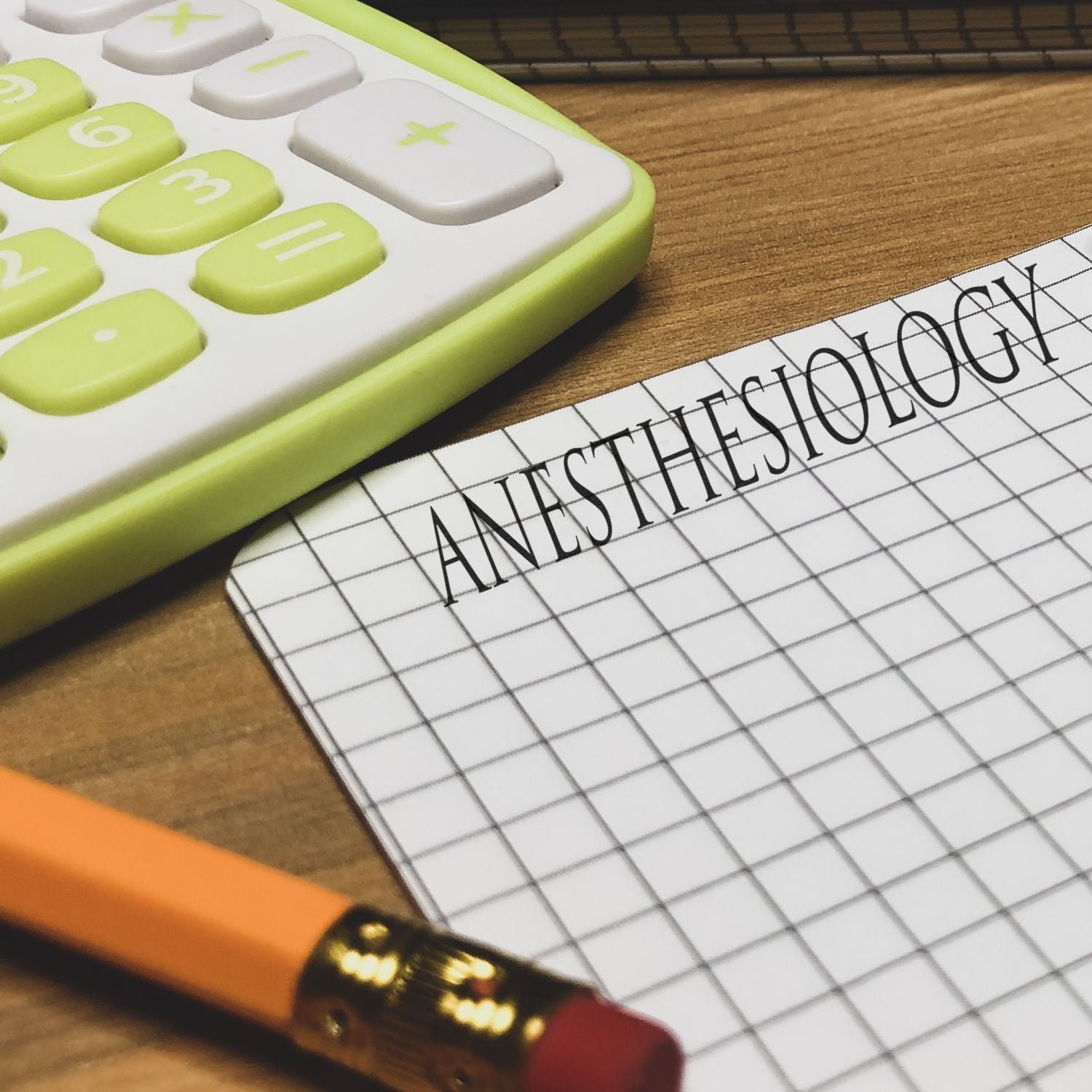 Large Anesthesiology Rubber Stamp imprint on graph paper, next to a pencil and a green calculator on a wooden desk.