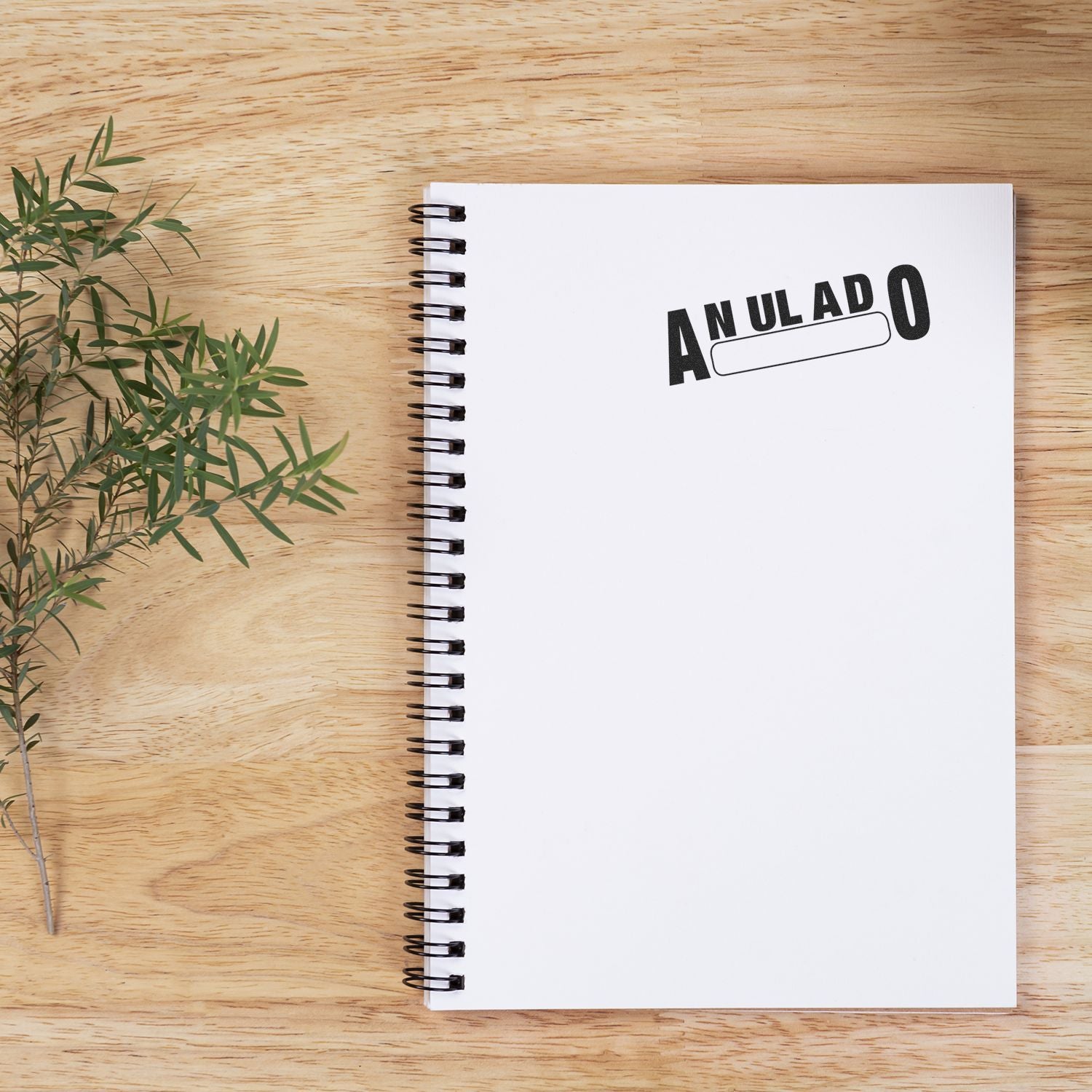 Large Self Inking Anulado Stamp used on a white spiral notebook placed on a wooden surface with a small plant on the side.