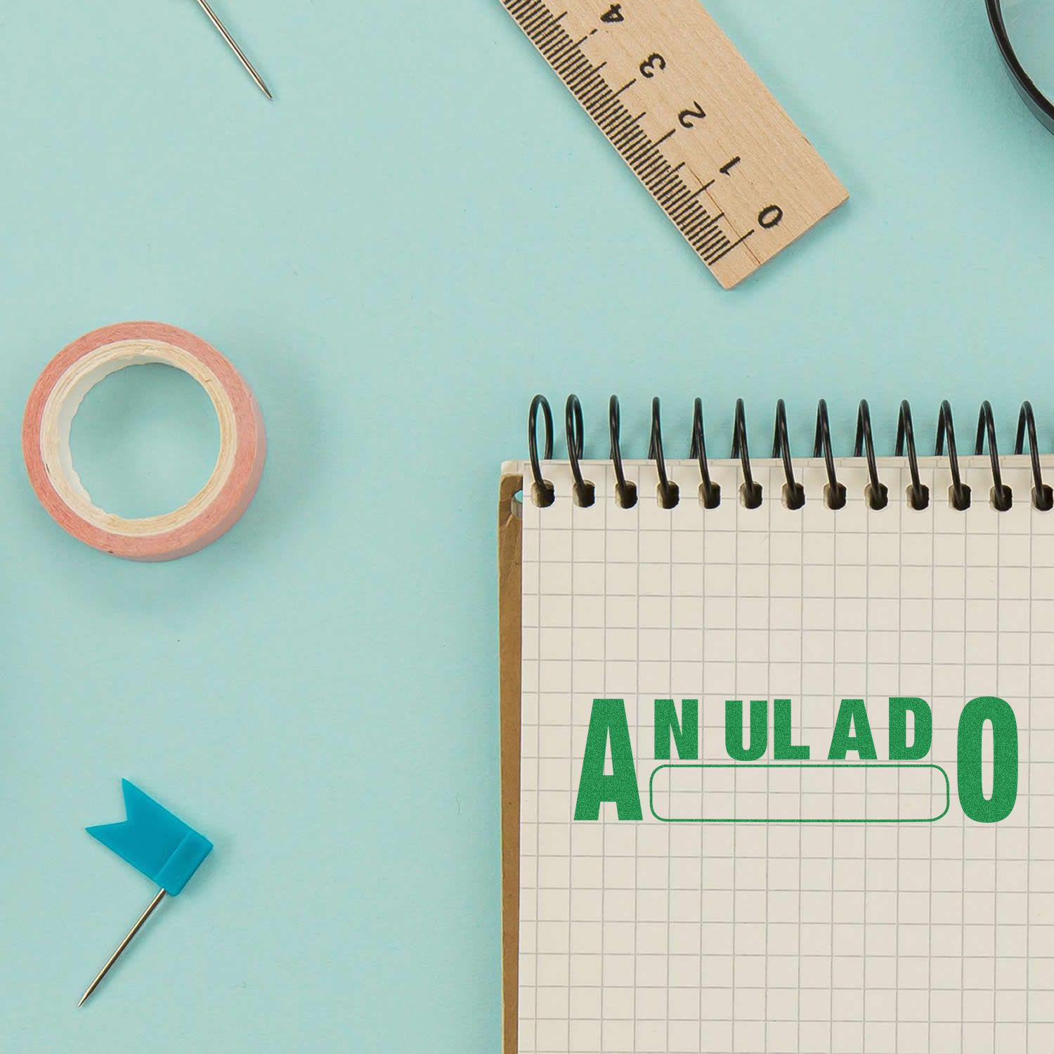 A Self Inking Anulado Stamp marks ANULADO in green on a spiral notebook, surrounded by office supplies on a light blue background.