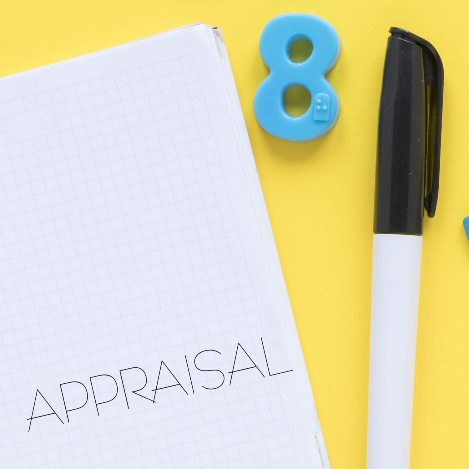 Self Inking Appraisal Stamp in use on a notebook with the word APPRAISAL stamped, alongside a pen and a blue number 8 on a yellow background.