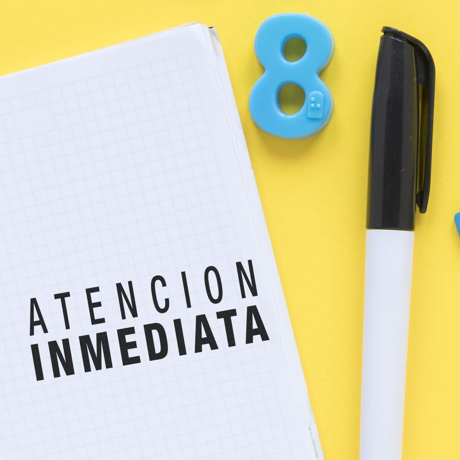 Atencion Inmediata rubber stamp on a notebook with a pen and a blue number 8 on a yellow background.