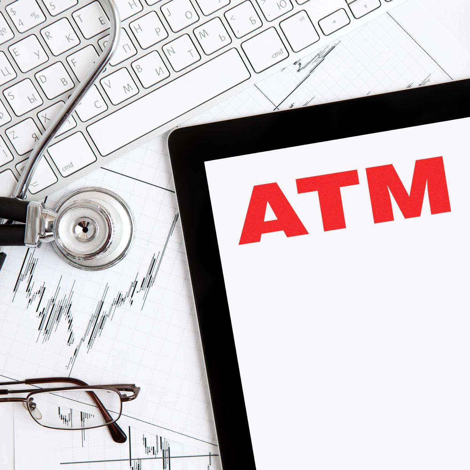 Large Self Inking ATM Stamp in use on a document, surrounded by a stethoscope, keyboard, glasses, and financial charts.