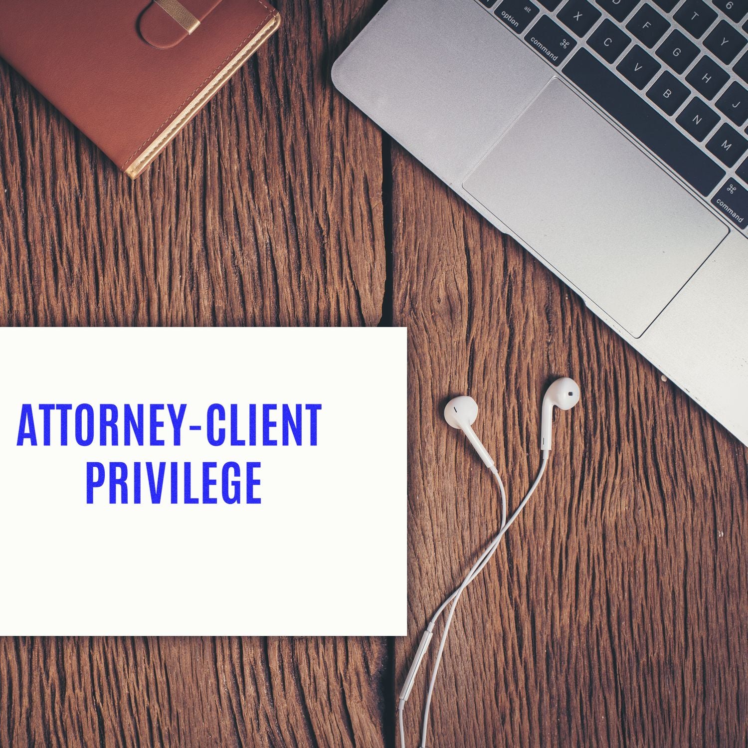 Attorney-Client Privilege rubber stamp on paper next to a laptop, earphones, and a notebook on a wooden desk.