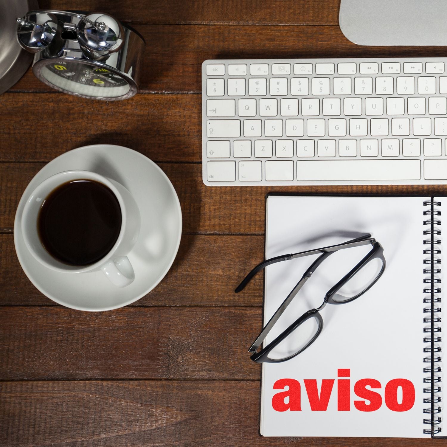 A desk with a keyboard, coffee, glasses, and a notebook with aviso stamped using the Self Inking Aviso Stamp.