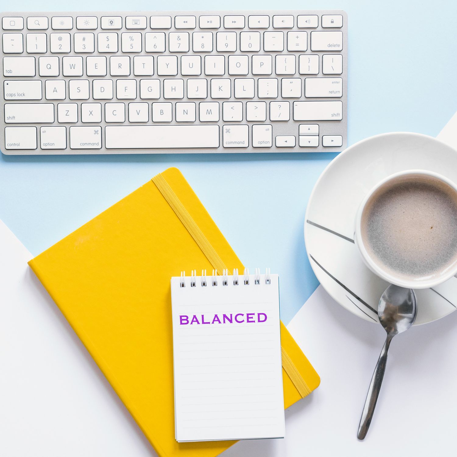 Balanced rubber stamp on a notepad with a keyboard, yellow notebook, and a cup of coffee on a desk.