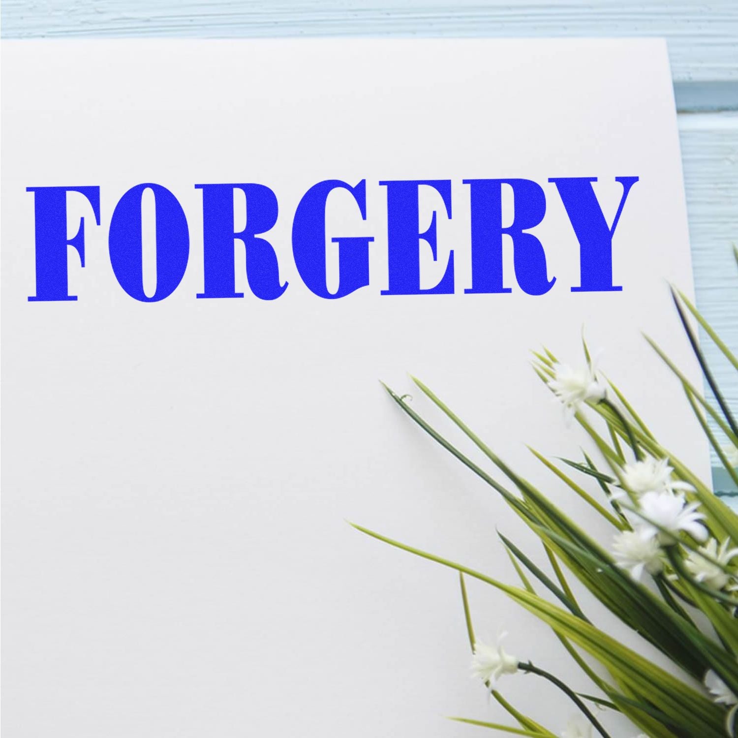 A white paper stamped with FORGERY in bold blue letters using the Self Inking Bank Forgery Stamp, next to green and white flowers.