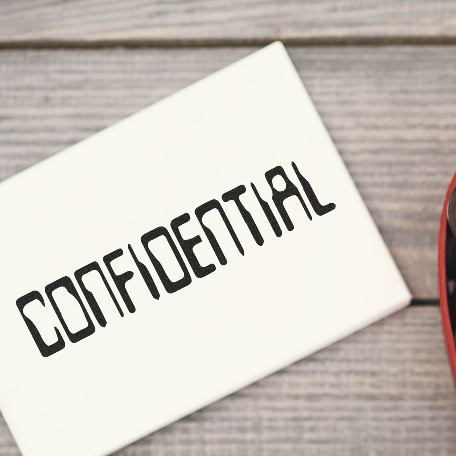 Large Barcode Confidential Rubber Stamp marking CONFIDENTIAL on a white envelope, placed on a wooden surface.