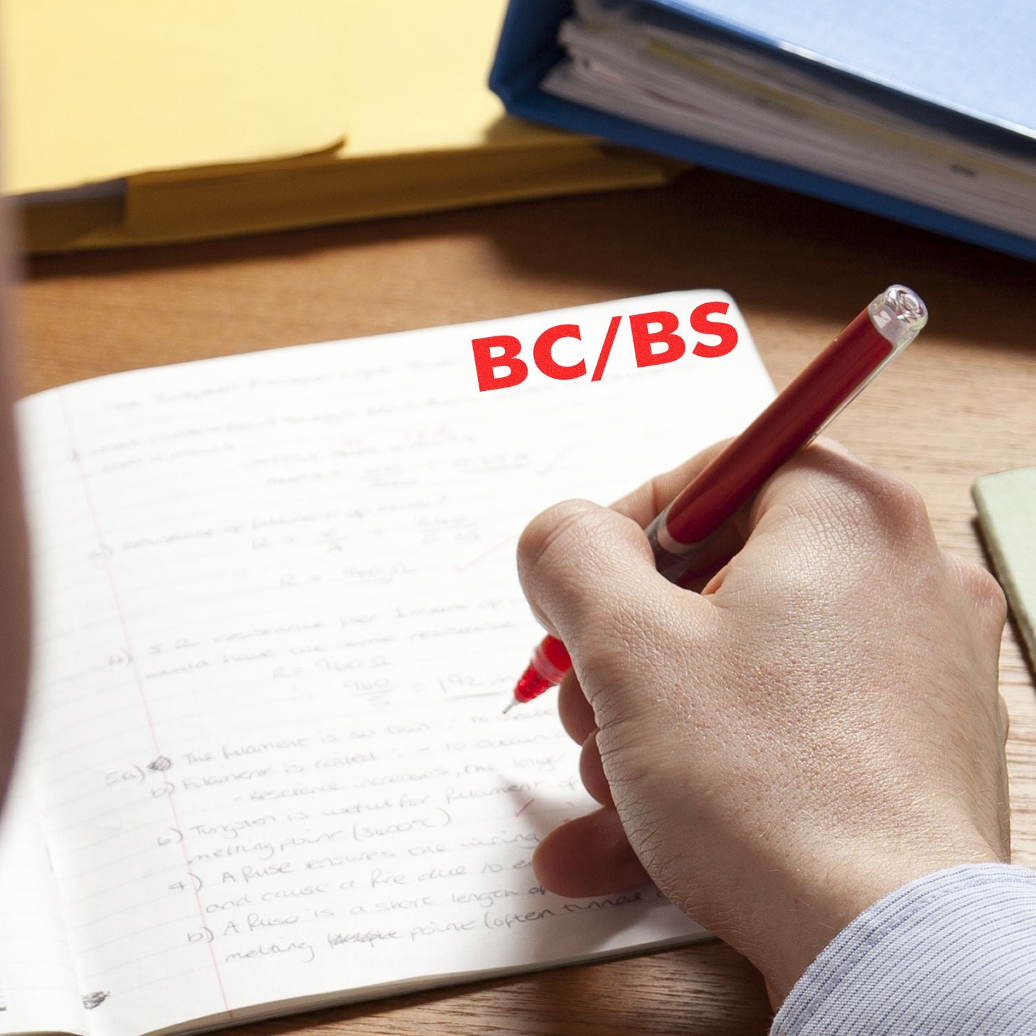 Hand holding a red pen writing in a notebook with a BC/BS Medical Provider Rubber Stamp impression in red ink on the page.