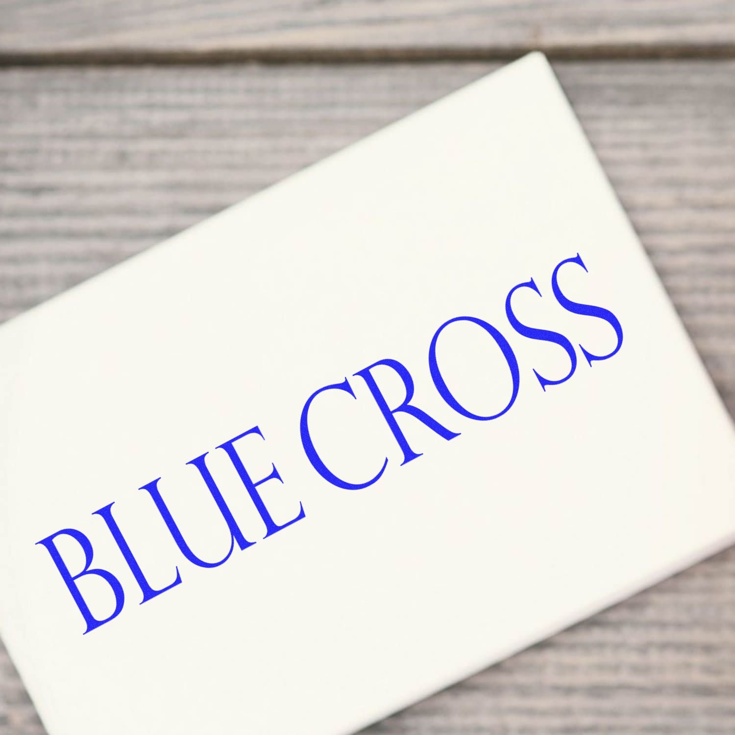 Blue Cross Rubber Stamp imprint on white paper, showcasing clear and bold blue text, placed on a wooden surface.