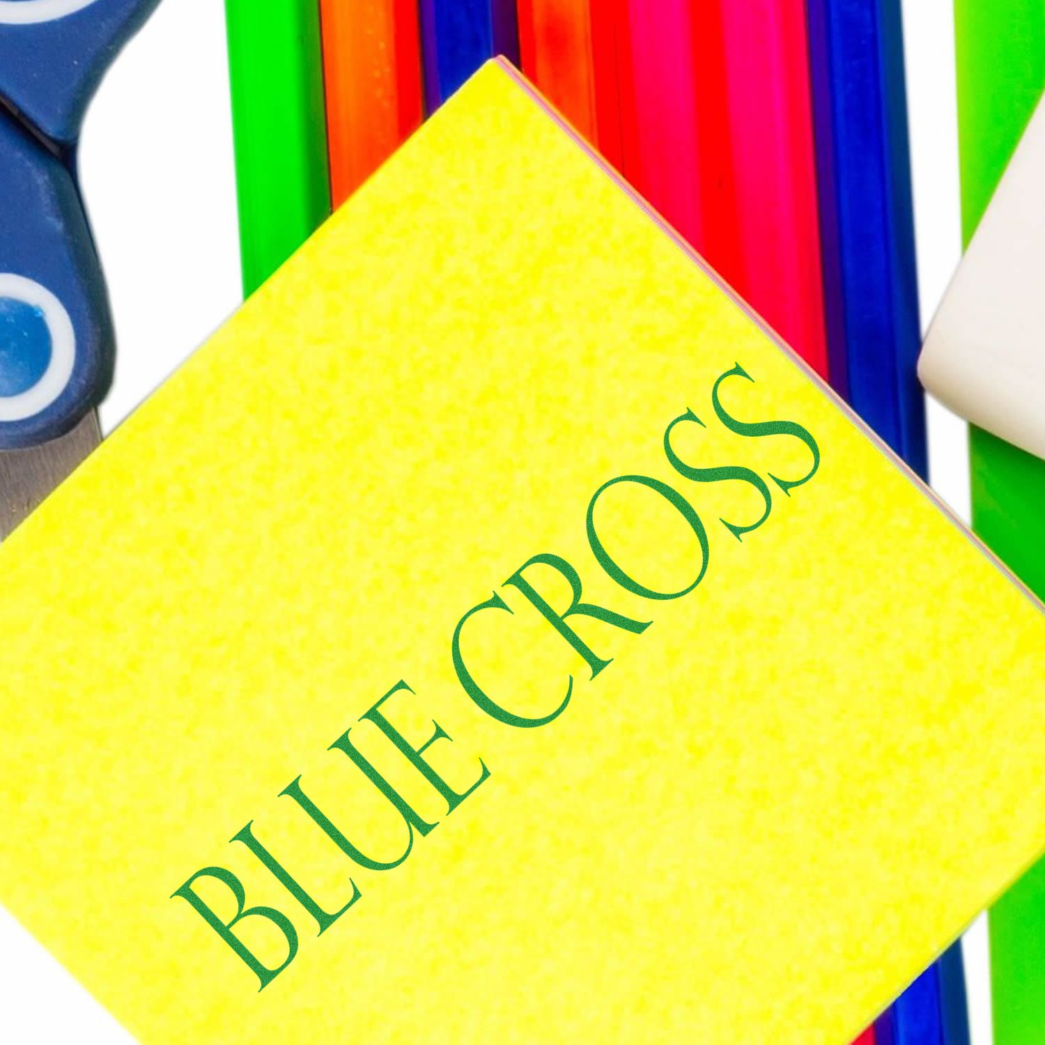 Large Pre-Inked Blue Cross Stamp in use, stamping BLUE CROSS on a bright yellow sticky note, surrounded by colorful office supplies.