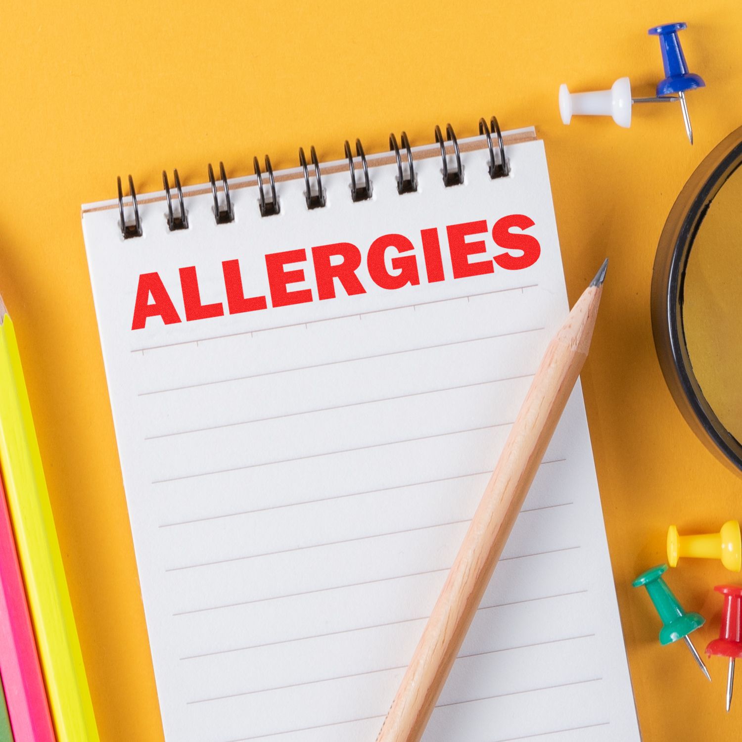 Bold Allergies Rubber Stamp in red ink on a notepad, surrounded by colorful push pins, pencils, and a magnifying glass.