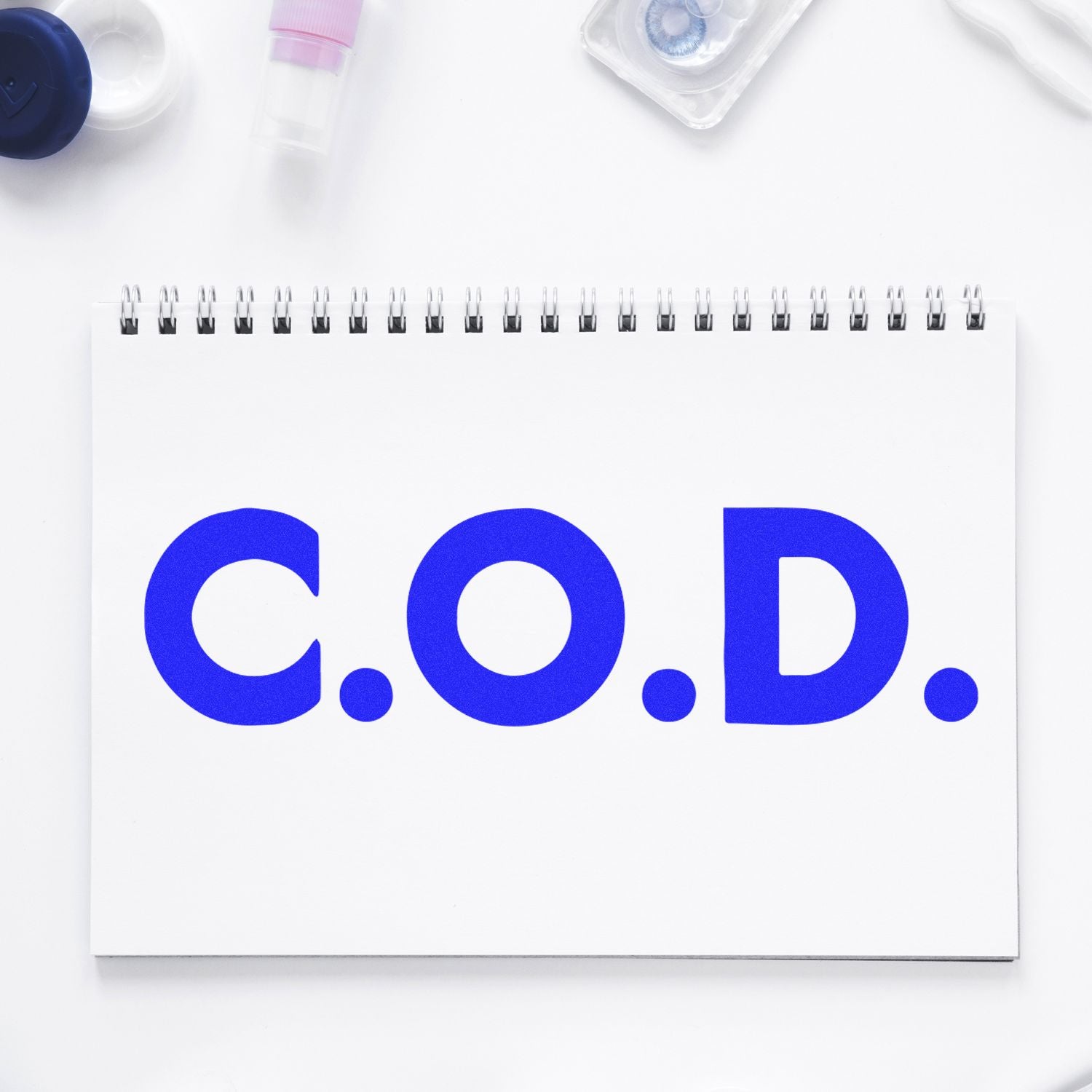 Large Pre-Inked Bold COD Stamp in use, displaying C.O.D. in bold blue letters on a white notepad, surrounded by office supplies.