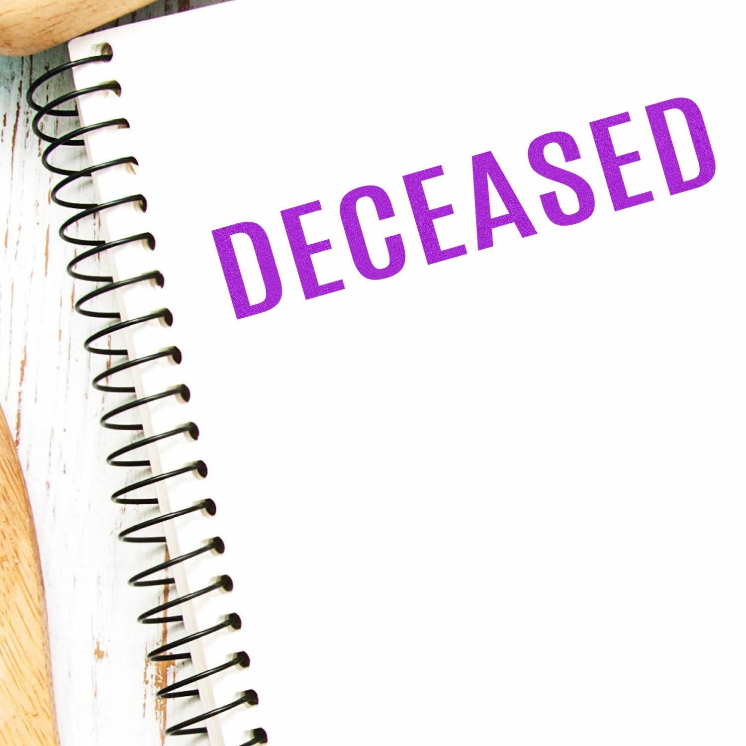 Spiral notebook with a bold DECEASED rubber stamp in purple ink on a white page, placed on a wooden surface.