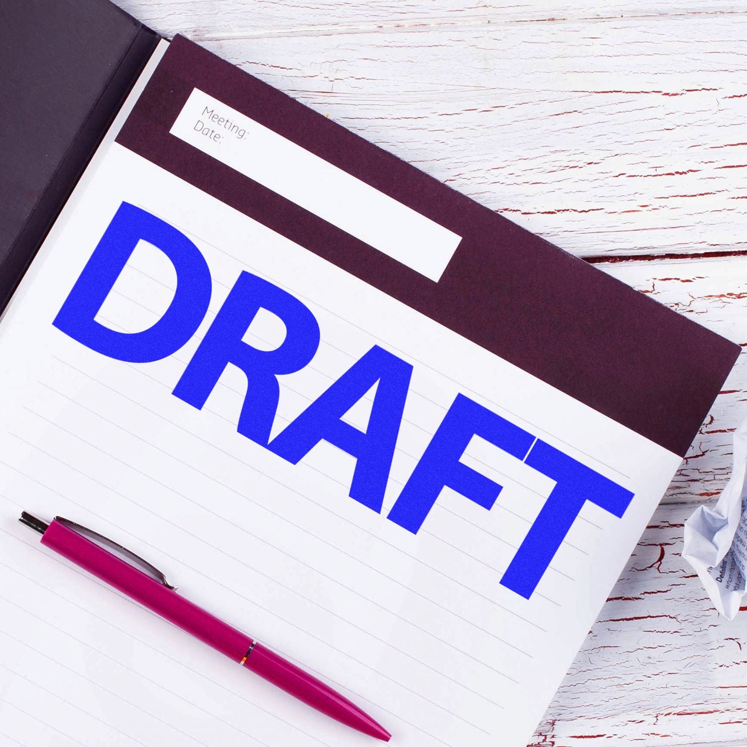 Notebook with a large blue 'DRAFT' stamped on a page using a Bold Draft Rubber Stamp, next to a red pen on a white wooden table.