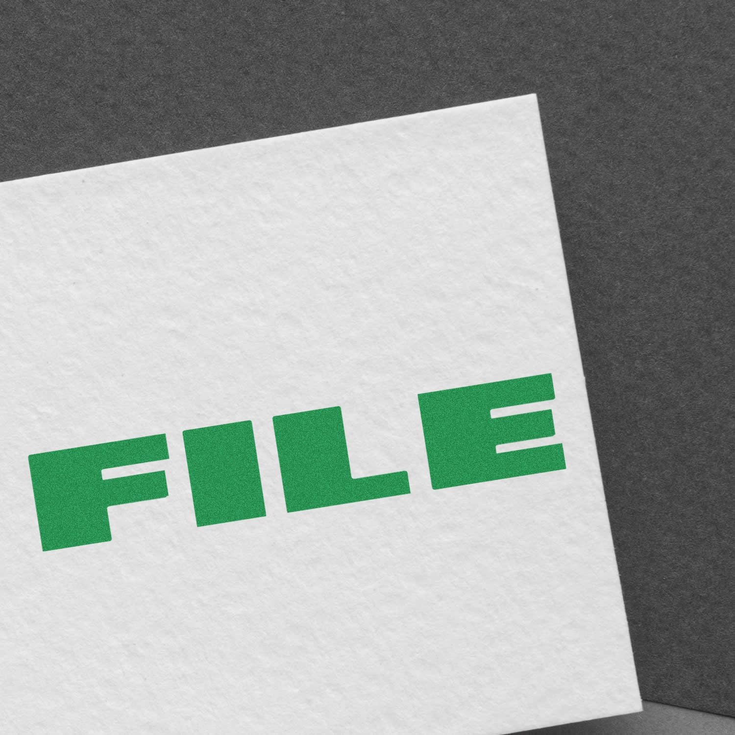 A white paper stamped with FILE in green ink using the Large Self Inking Bold Font File Stamp, placed on a dark gray surface.