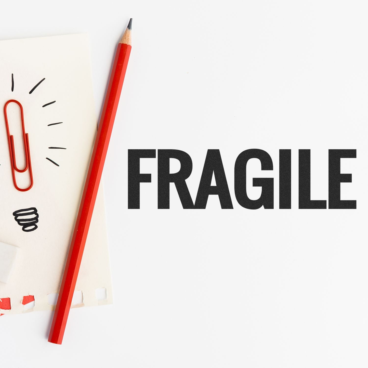 Red pencil and paperclip on paper next to the Bold Fragile Rubber Stamp imprint reading FRAGILE in bold black letters.