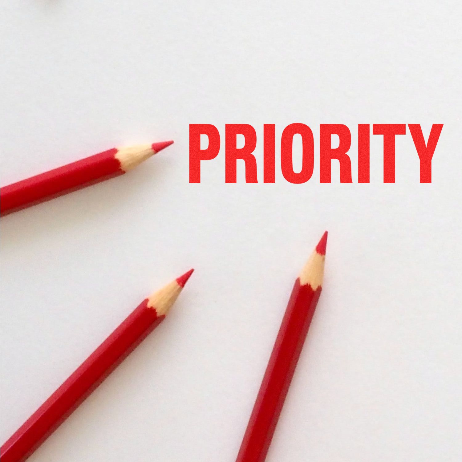 Three red pencils pointing towards the Large Self Inking Bold Priority Stamp mark on white paper with the word PRIORITY in bold red letters.