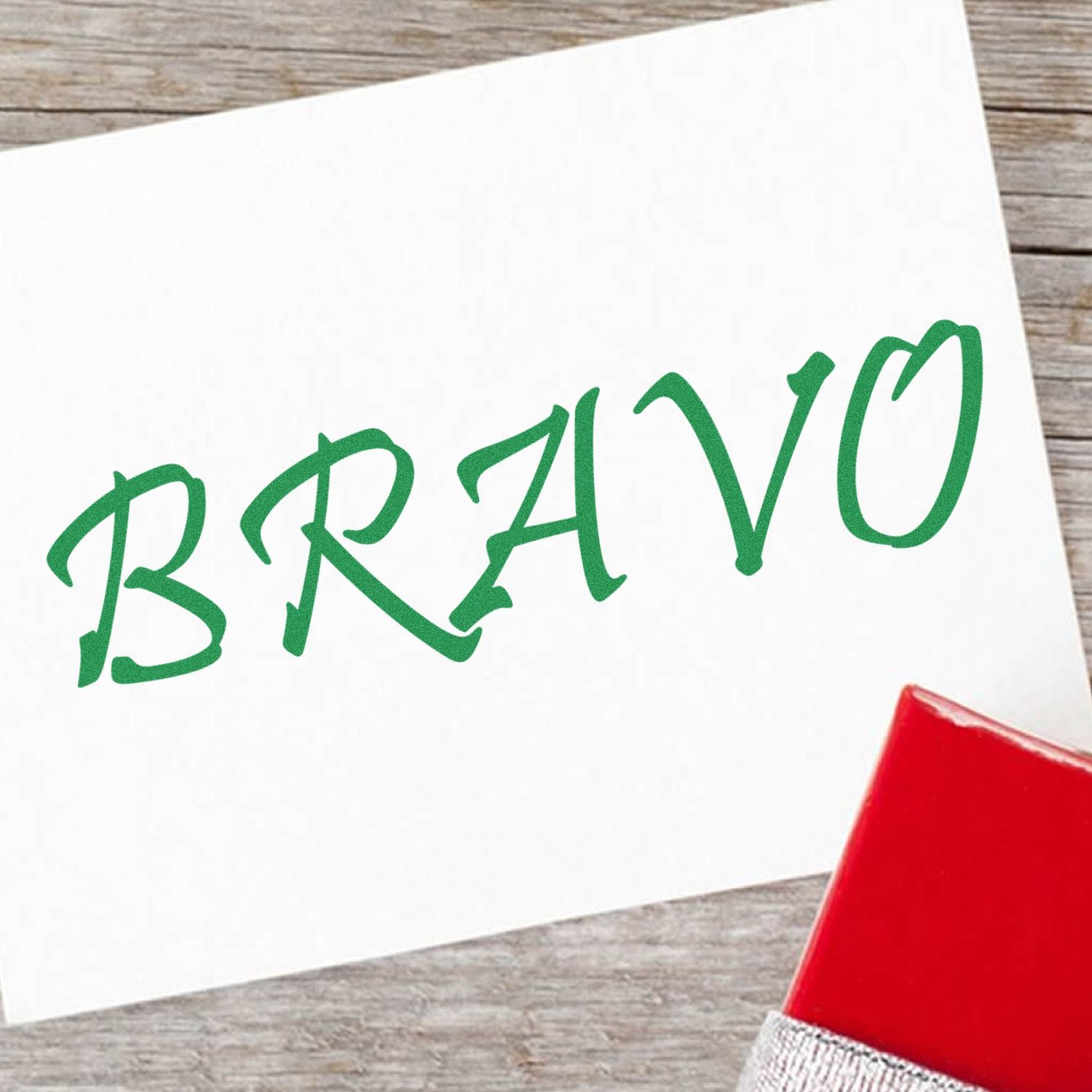 Bravo Rubber Stamp in green ink on white paper, with a red stamp handle visible on a wooden surface.