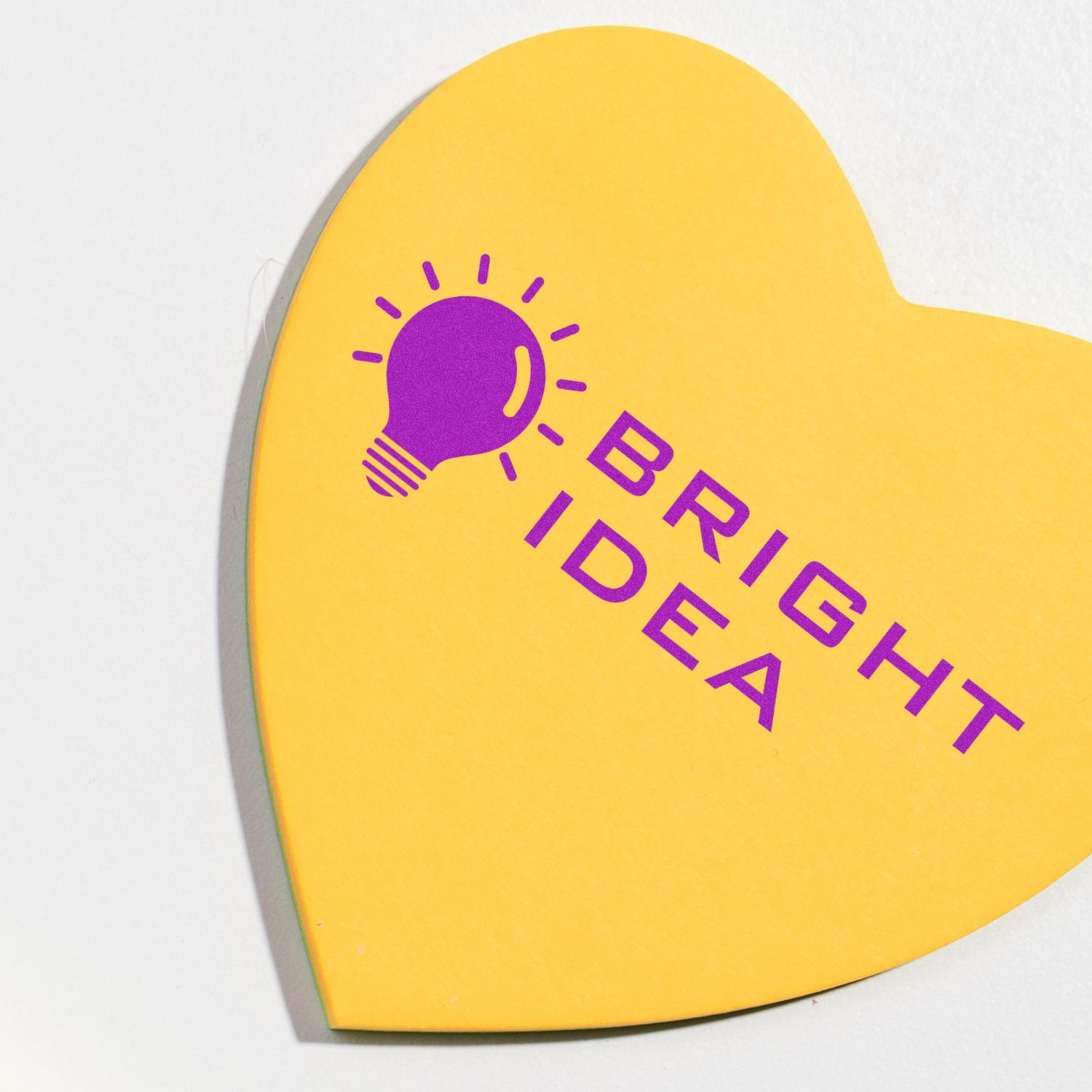 Yellow heart-shaped paper with a purple light bulb and the text Bright Idea stamped on it.