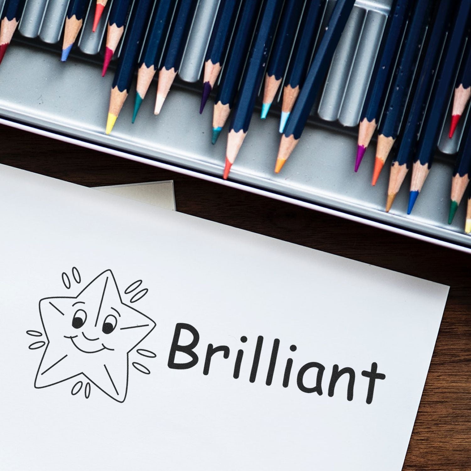 Brilliant Rubber Stamp with a smiling star and the word 'Brilliant' stamped on paper, colored pencils in the background.