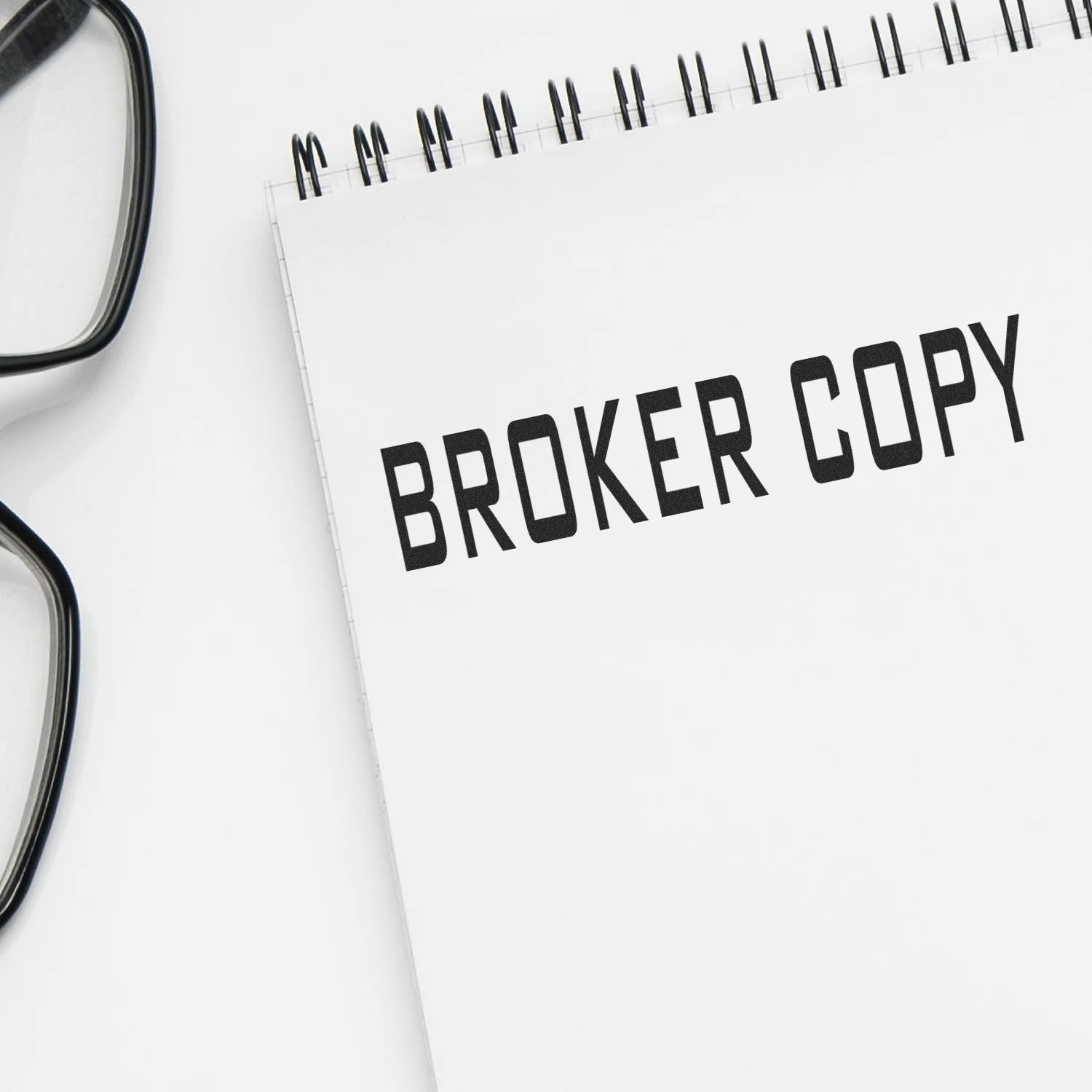 A notebook stamped with "BROKER COPY" using the Broker Copy Rubber Stamp, placed next to a pair of black-framed glasses.