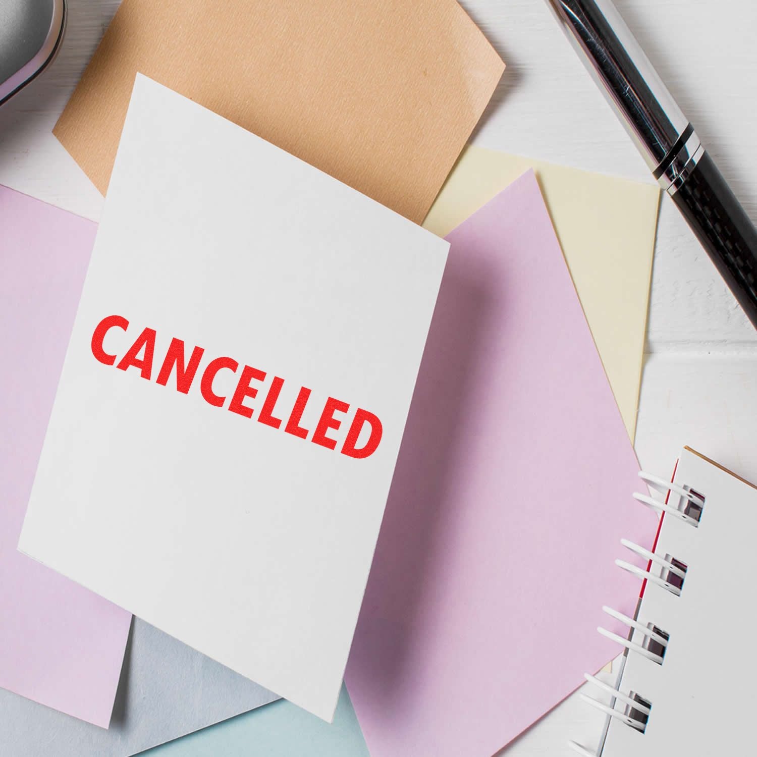 Cancelled Rubber Stamp used on a white paper surrounded by colorful sheets, a pen, and a notebook on a desk.