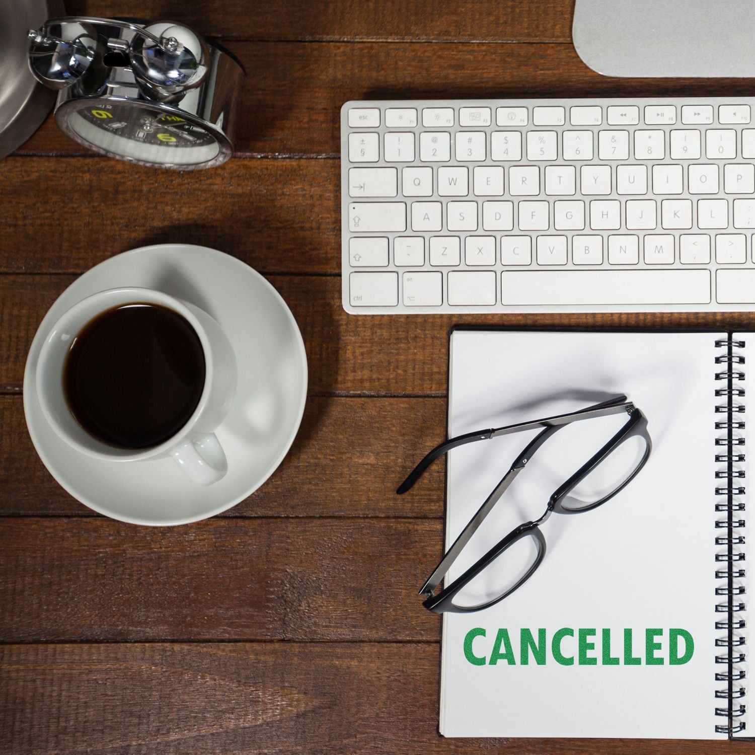 Desk with keyboard, coffee, glasses, and notebook stamped with a green 'Cancelled' rubber stamp.