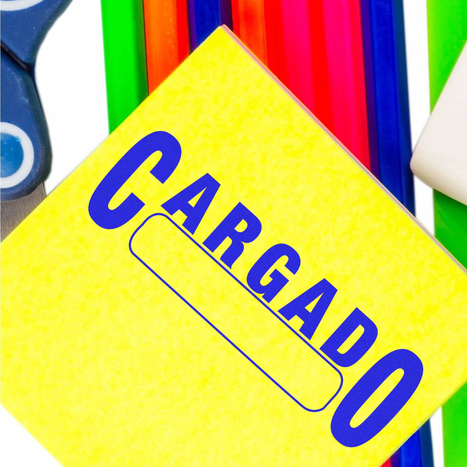 Large Cargado Rubber Stamp in blue ink on a yellow paper, surrounded by colorful stationery items including scissors and rulers.